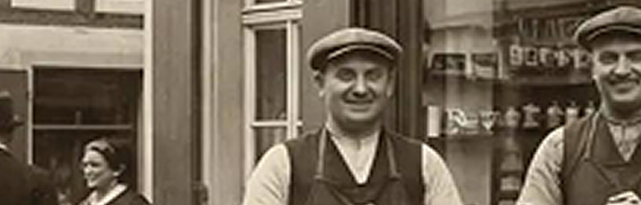 Sepiafarbenes historisches Straßenfoto mit zwei Männern in Arbeitskleidung vor einem Laden in der Stadt