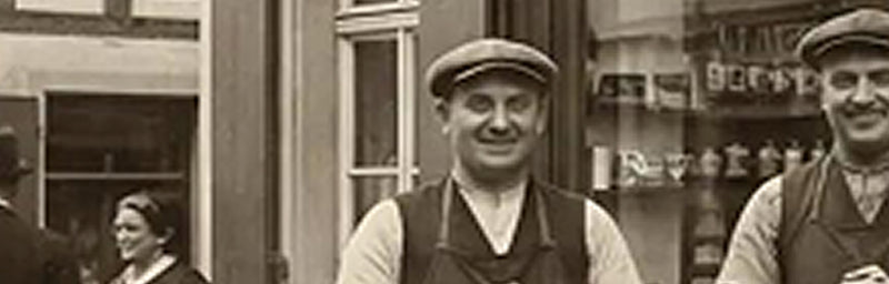 Sepiafarbenes historisches Straßenfoto mit zwei Männern in Arbeitskleidung vor einem Laden in der Stadt