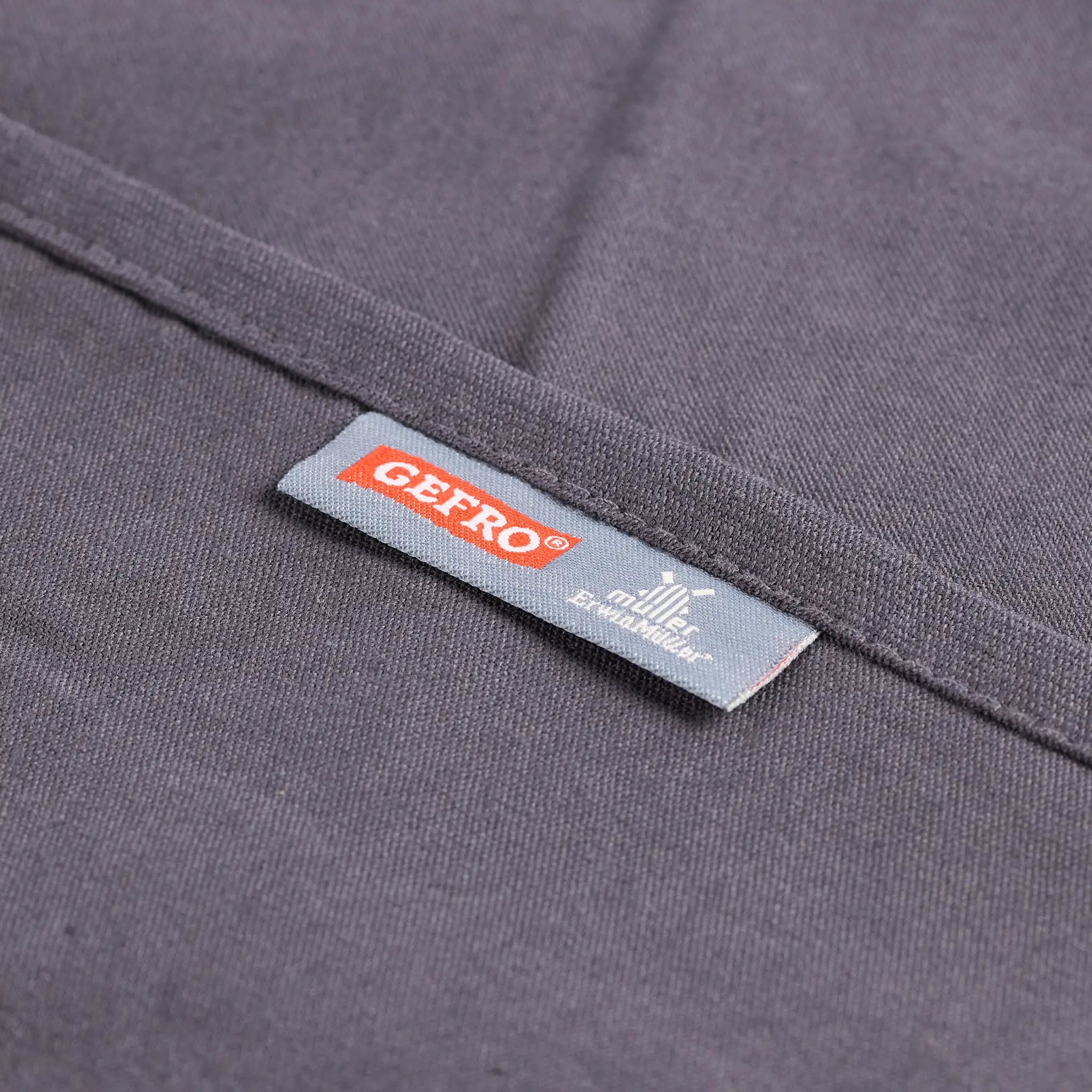 Nahaufnahme von grauem Stoff mit eingenähtem GEFRO-Label, zeigt Material und saubere Verarbeitung des Produkts.