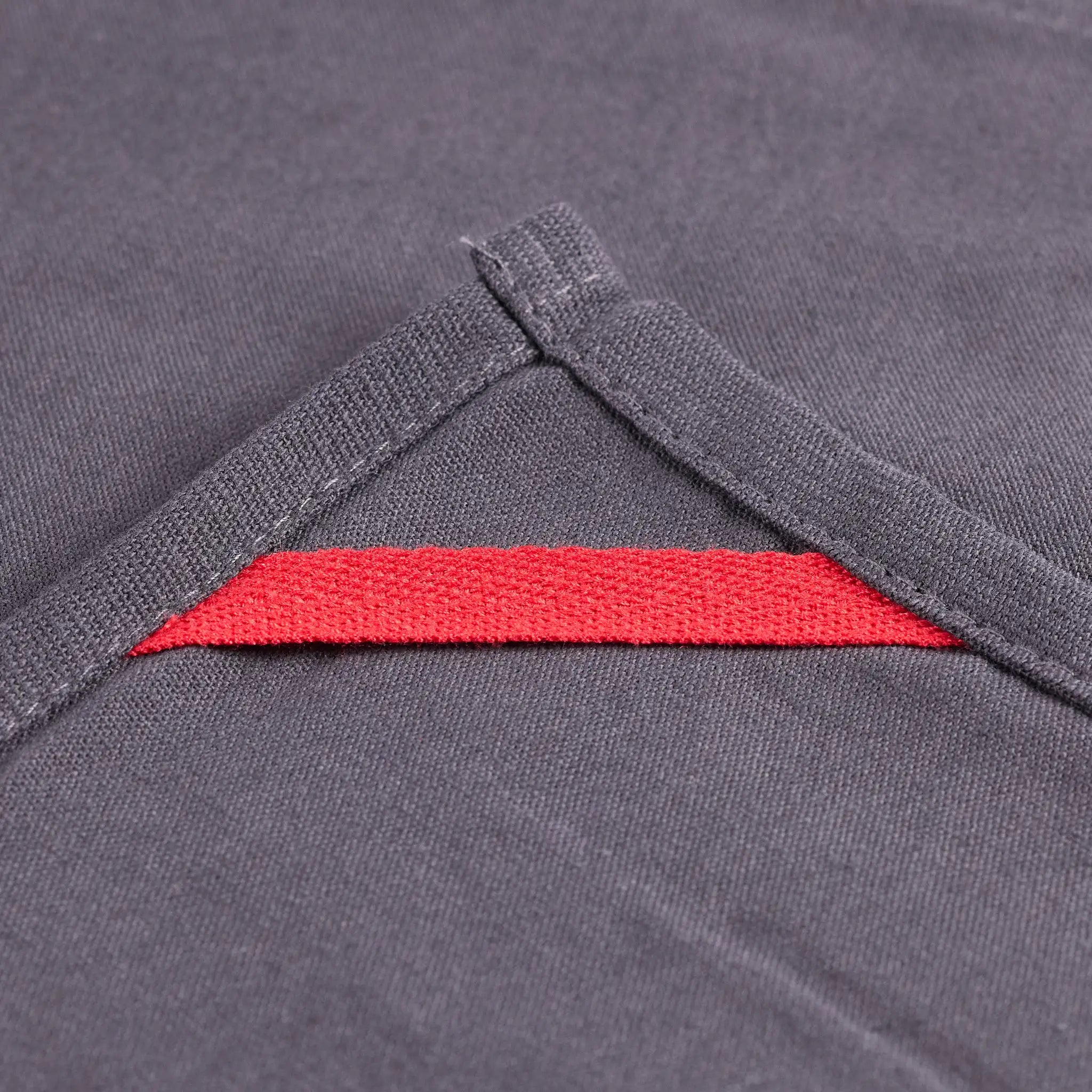 Nahaufnahme eines grauen Stoffdetails mit rotem Einsatz und überkreuzten Nähten an einem Kleidungsstück.