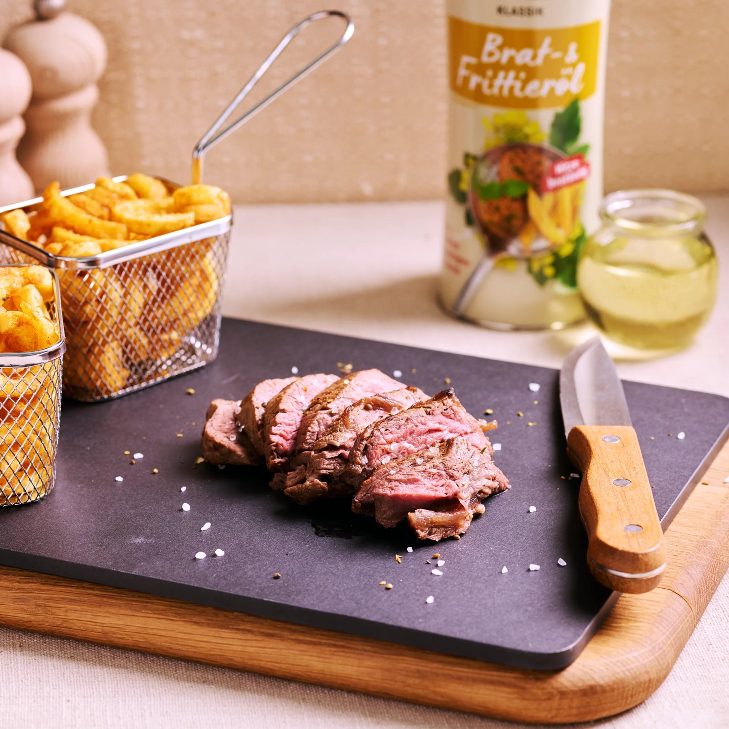 Geschnittenes Steak auf schwarzer Platte mit Pommes, Messer und Brat- und Frittieröl im Hintergrund