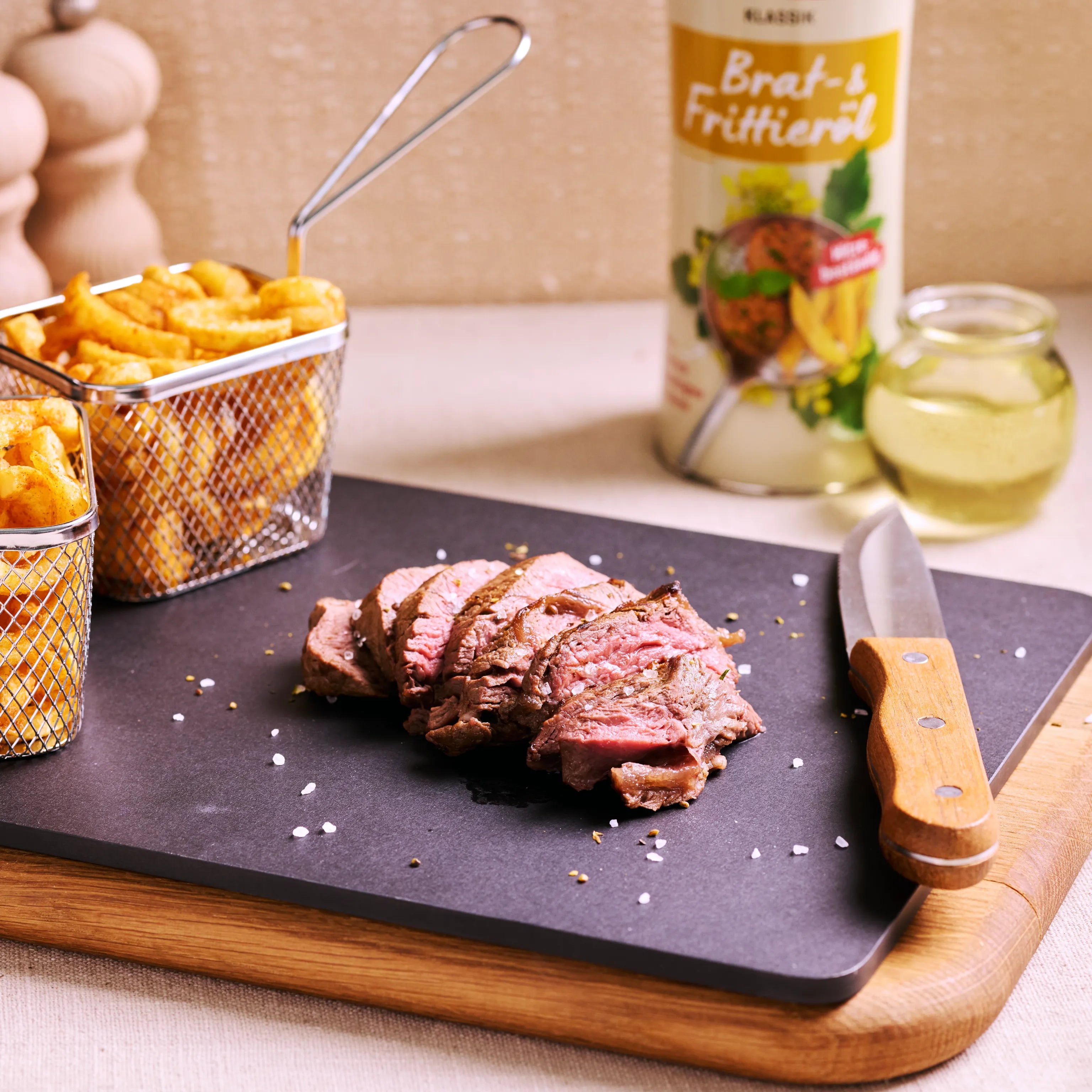 Geschnittenes Steak auf schwarzer Platte mit Pommes, Messer und Brat- und Frittieröl im Hintergrund