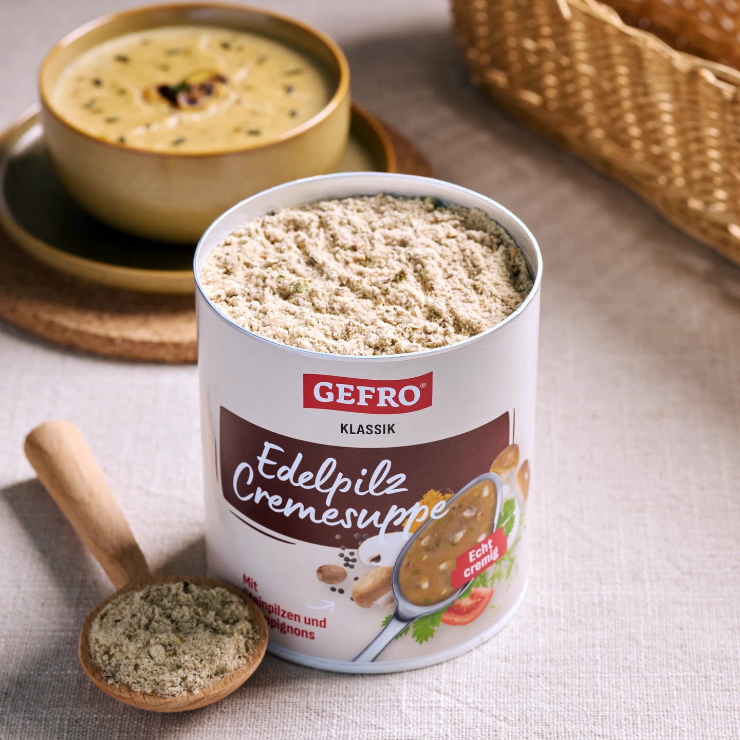 Offene Dose GEFRO Edelpilz Cremesuppe mit Pulver und Holzlöffel, dahinter eine Schale mit servierter Suppe