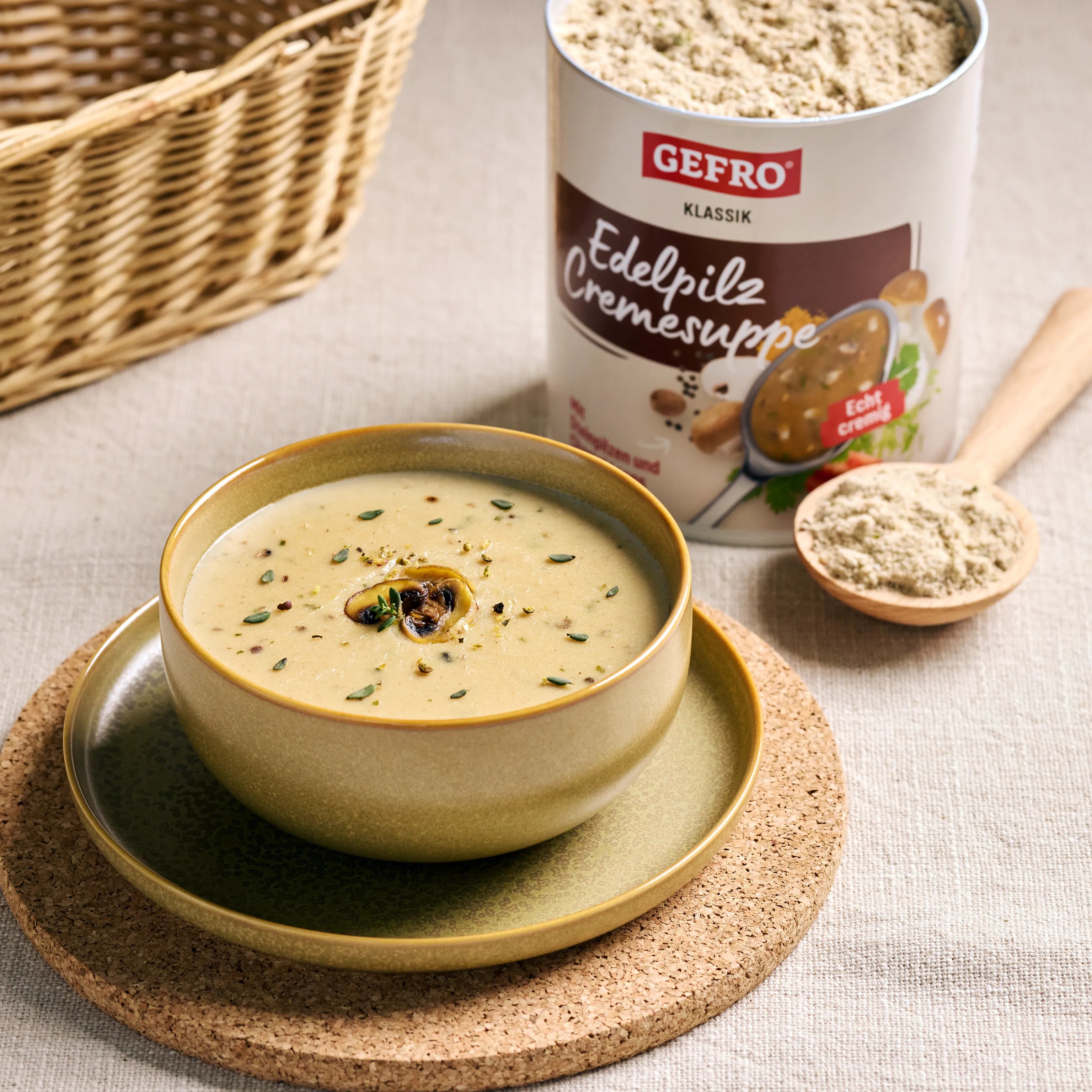 Schale mit cremiger Pilzsuppe auf Unterteller, daneben Dose GEFRO Edelpilz Cremesuppe und ein Löffel Pulver.