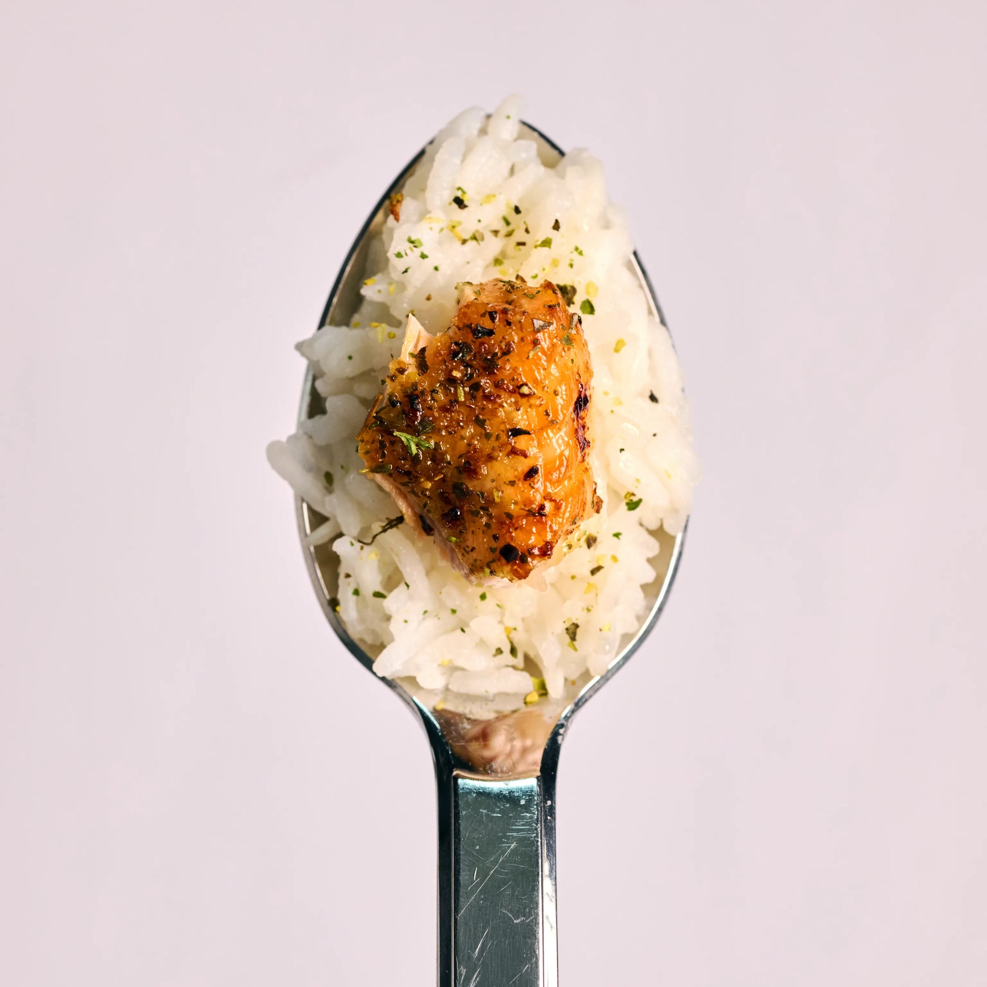 Löffel mit weißem Reis und einem gewürzten Stück Lachs, Nahaufnahme auf hellem Hintergrund für Food-Präsentation