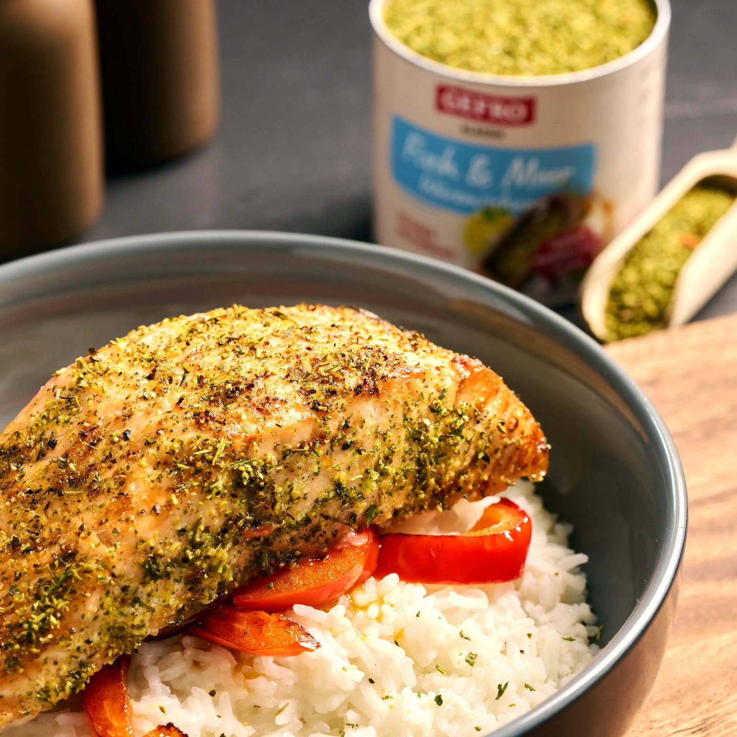 Gebratenes Lachsfilet mit grüner Kräuterwürze auf Reis und Paprika in einer Schüssel, Gewürzdose im Hintergrund