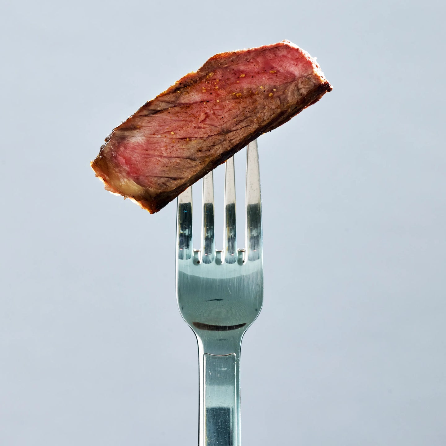 Nahaufnahme eines rosa gebratenen Steakstücks auf einer Gabel, saftig mit gebräunter Kruste vor hellem Hintergrund