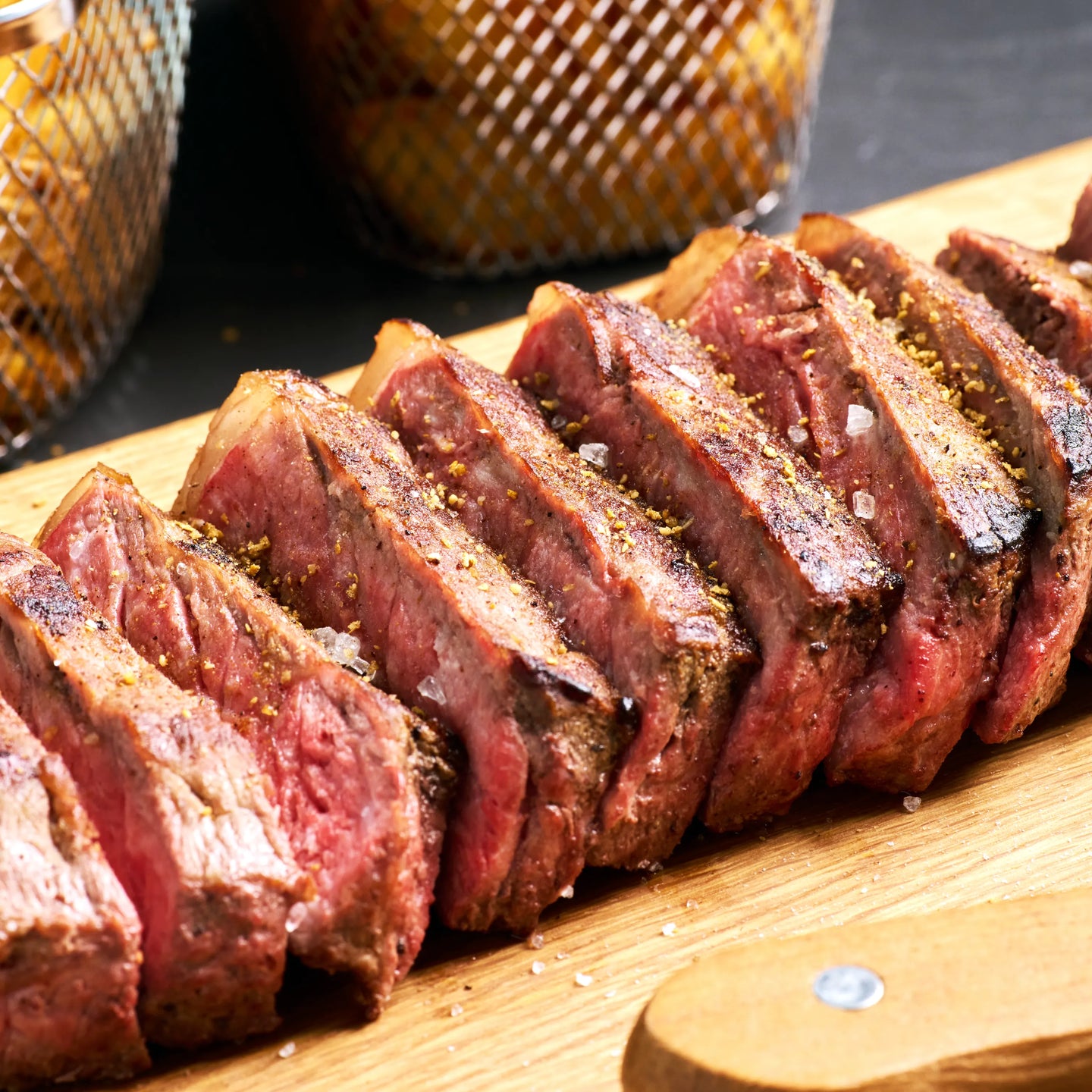 In Scheiben geschnittenes, rosa gebratenes Steak auf Holzbrett, mit grobem Salz gewürzt und servierfertig angerichtet