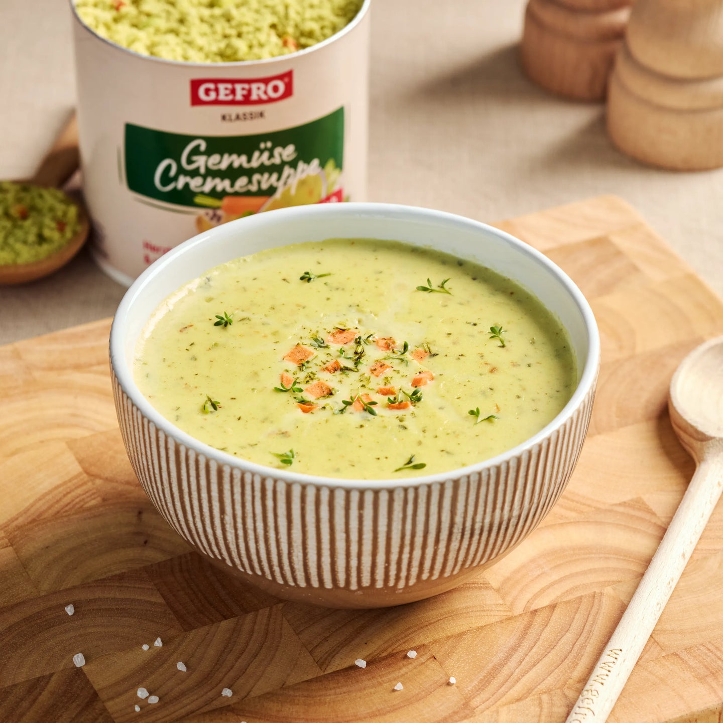 Schüssel mit cremiger Gemüsesuppe auf Holzbrett, dahinter Dose von Gefro Gemüsesuppe und ein Holzlöffel.