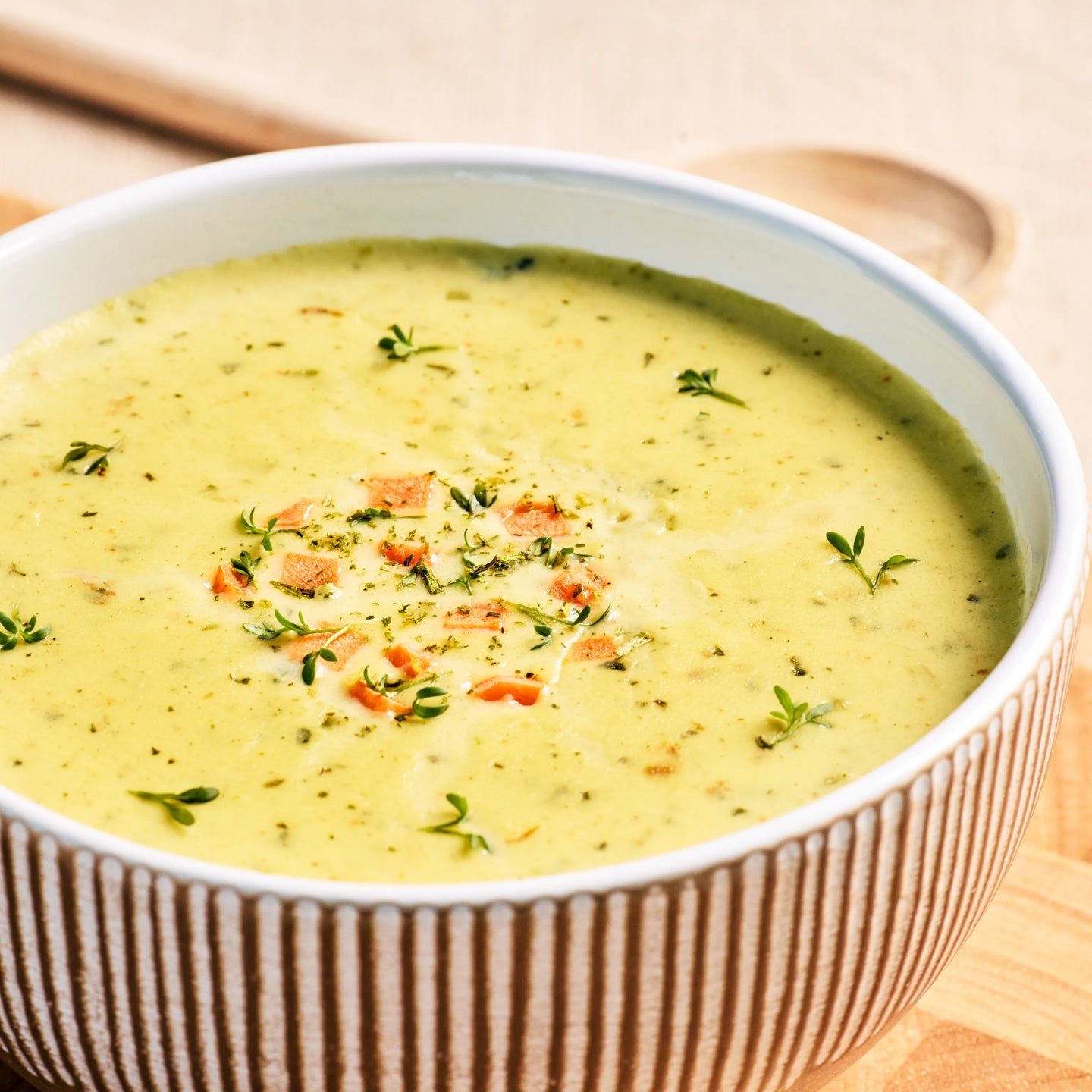 Schüssel mit cremiger Gemüsesuppe, garniert mit Kräutern und kleinen Karottenstücken, auf hellem Holztisch