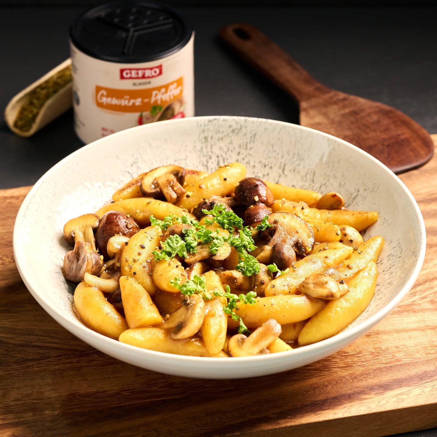 Schupfnudeln mit gebratenen Champignons und Petersilie in einer Schale, serviert auf Holzbrett in Küchenszene