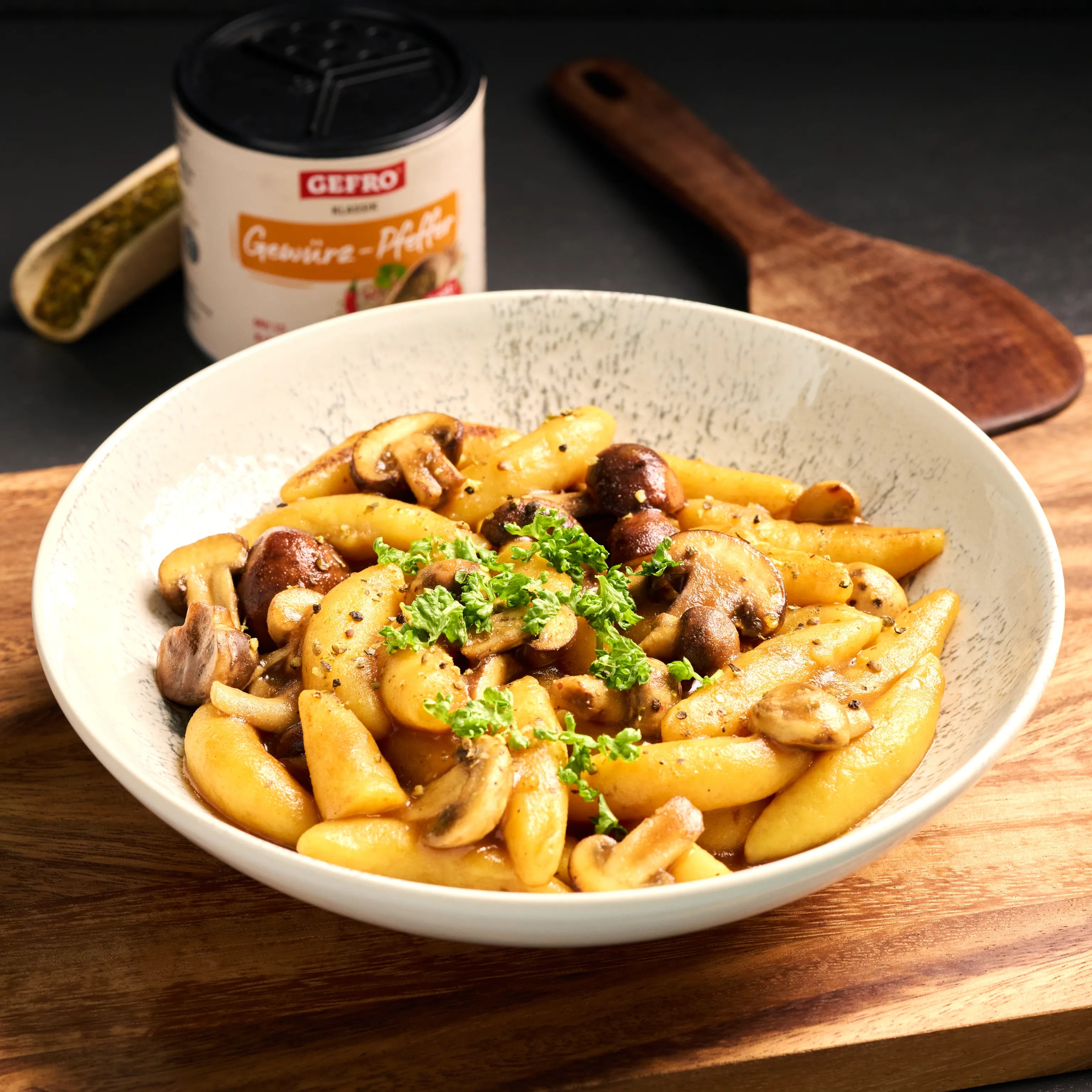 Schupfnudeln mit gebratenen Champignons und Petersilie in einer Schale, serviert auf Holzbrett in Küchenszene