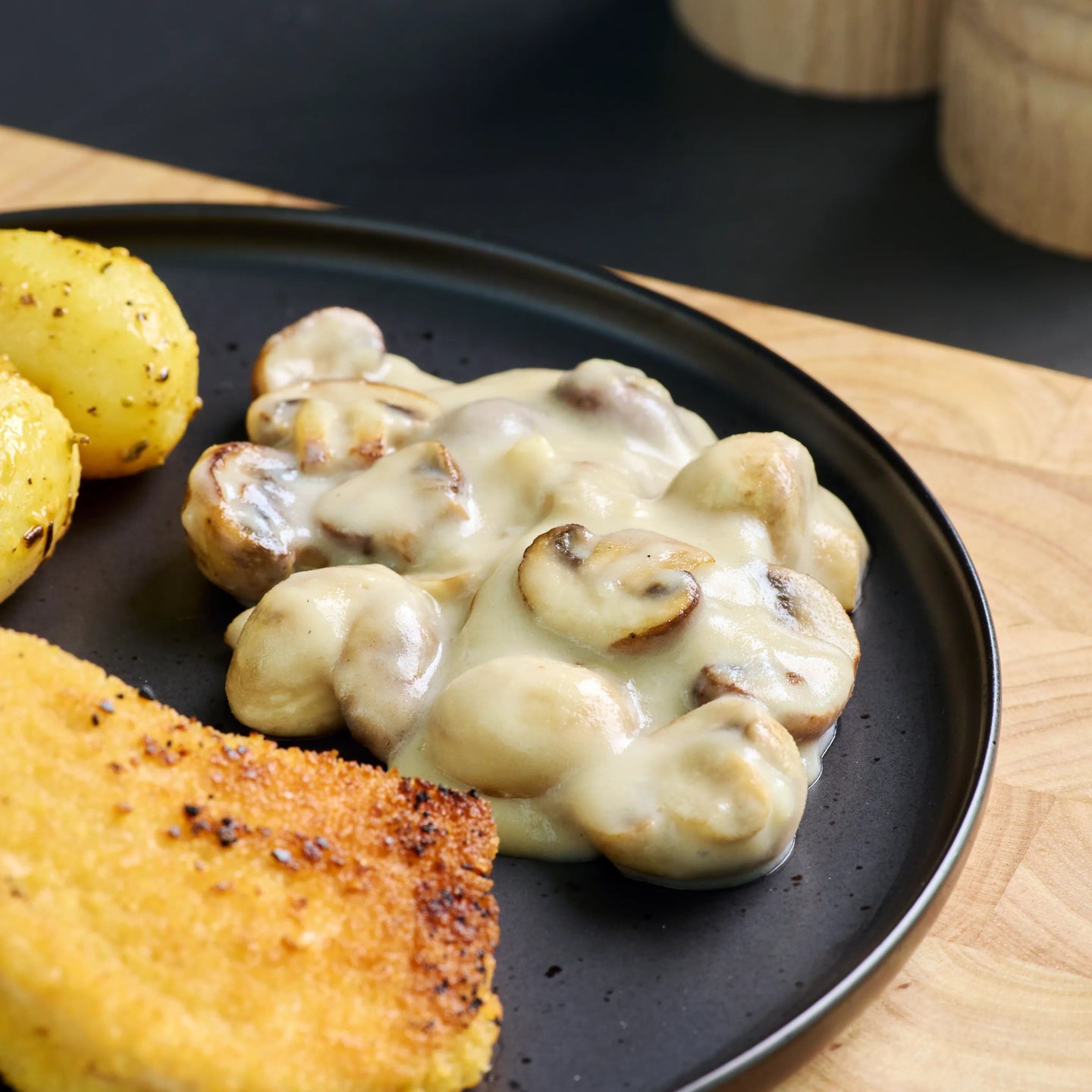 Panierte Schnitzel mit Champignons in heller Sauce und Kartoffeln auf schwarzem Teller serviert