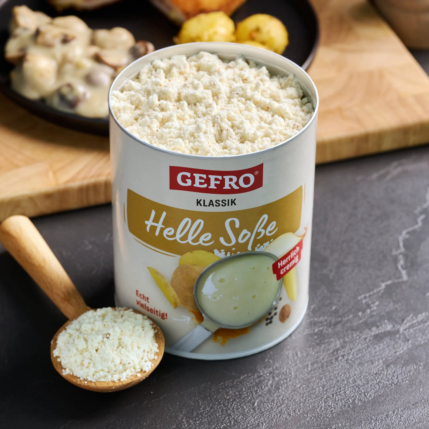 Dose GEFRO Klassik Helle Soße mit cremigem Soßenpulver, daneben ein Holzlöffel mit Pulver auf dem Tisch.