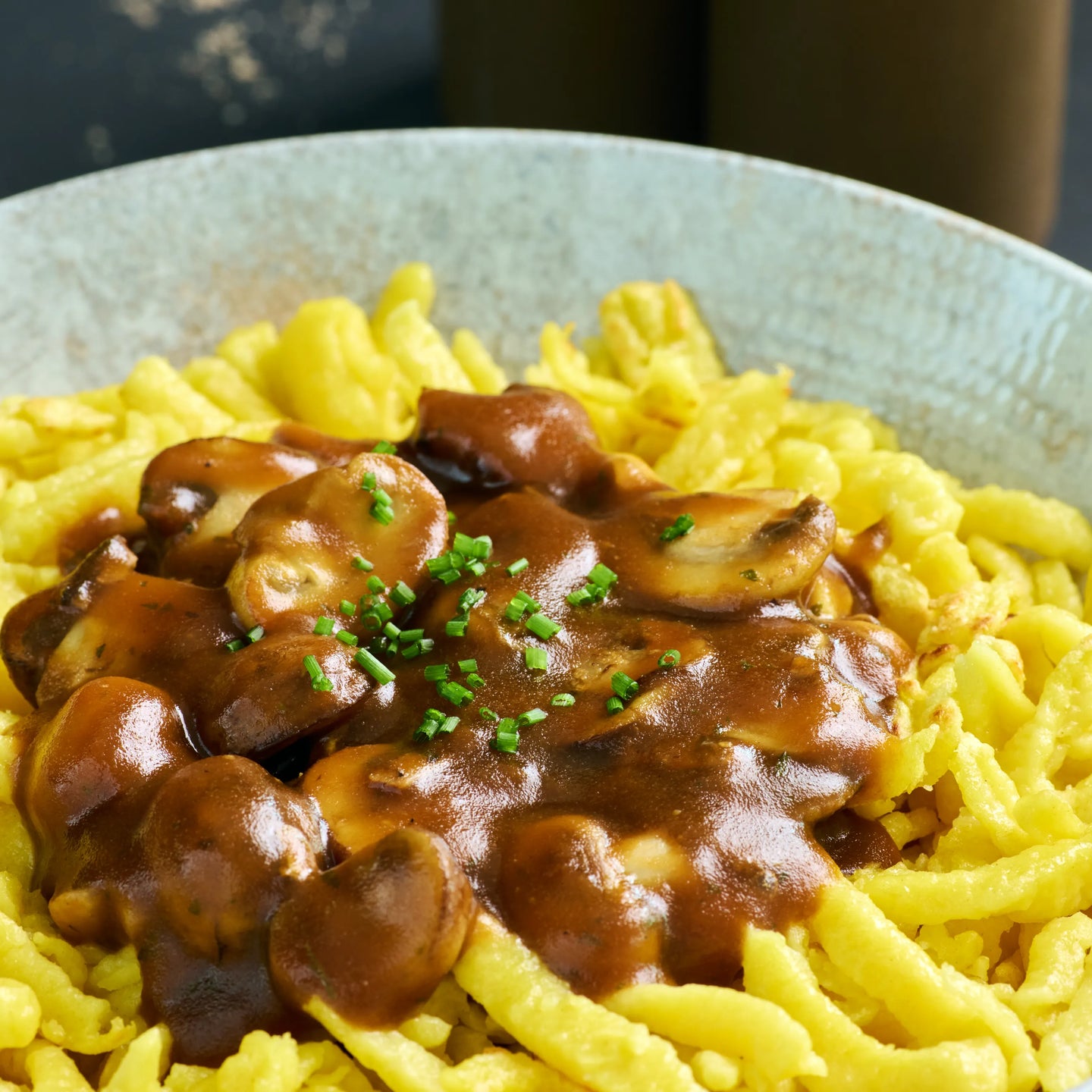 Spätzle mit brauner Pilzsoße und frischen Kräutern auf einem Teller, nah aufgenommen als appetitliches Hauptgericht