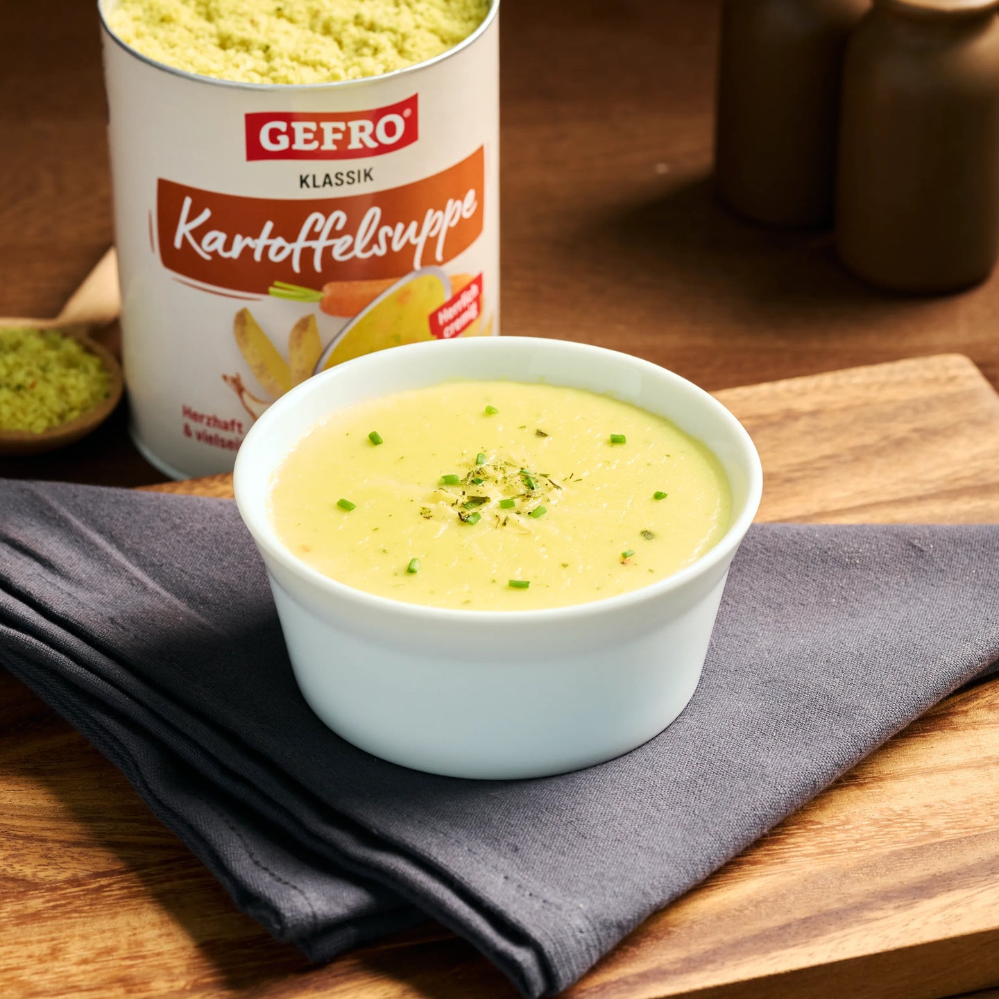Schale mit cremiger Kartoffelsuppe auf Holzbrett, daneben Dose GEFRO Klassik Kartoffelsuppe.