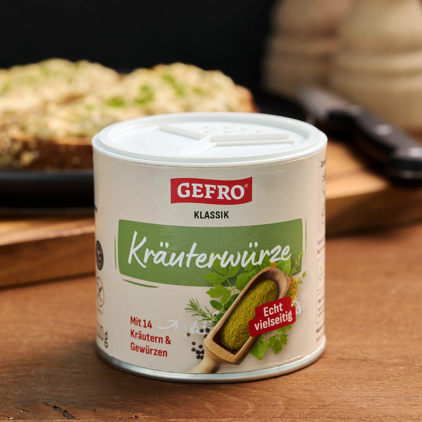 Dose GEFRO Klassik Kräuterwürze auf Holztisch, vorne gezeigt, mit unscharfem Gericht im Hintergrund