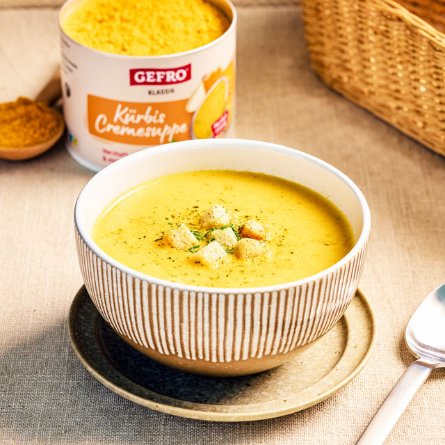 Schale mit cremiger Kürbissuppe und Croutons, dahinter Dose der GEFRO Kürbis Cremesuppe auf dem Tisch