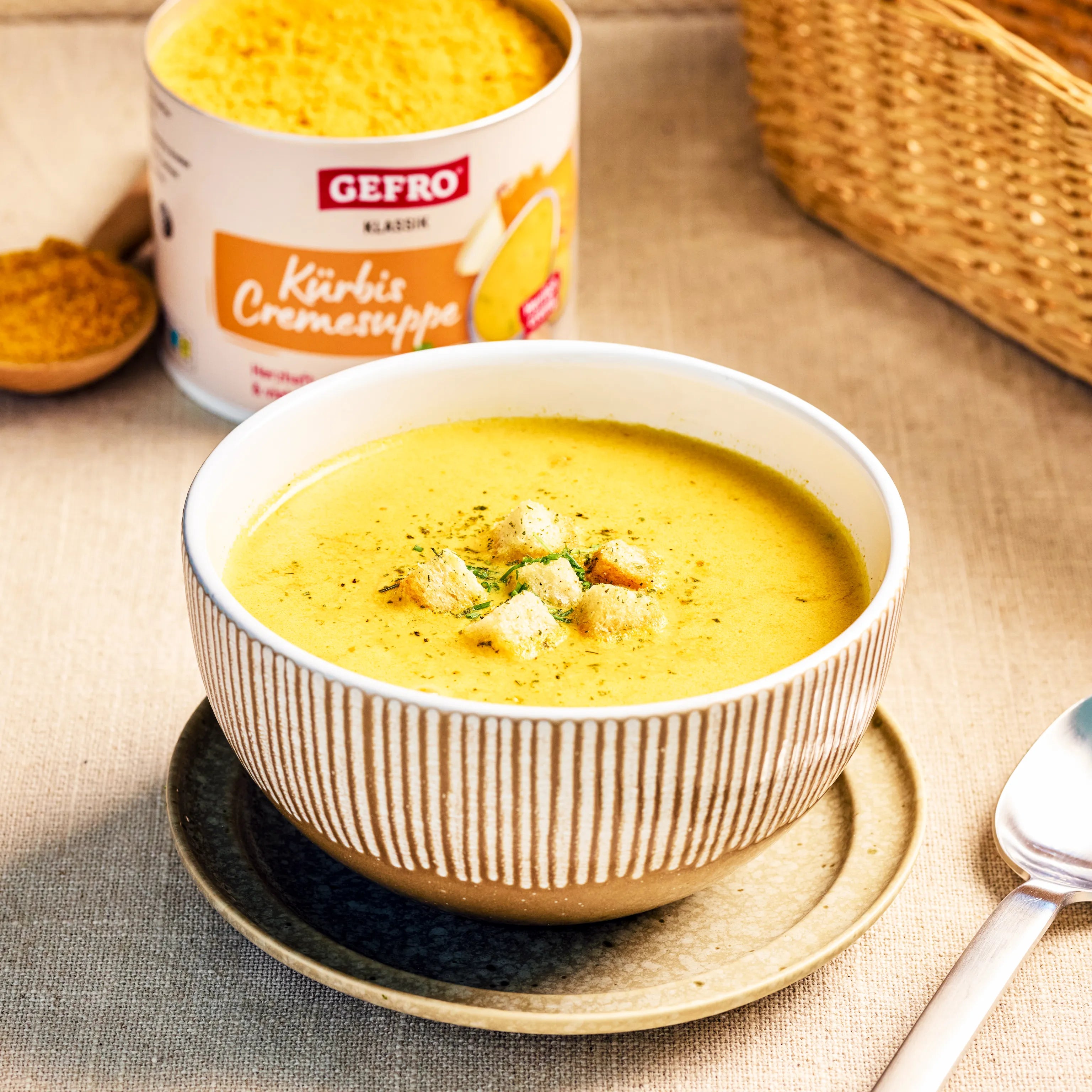 Schüssel mit cremiger Kürbissuppe und Croutons, dahinter eine Dose GEFRO Kürbis Cremesuppe auf dem Tisch