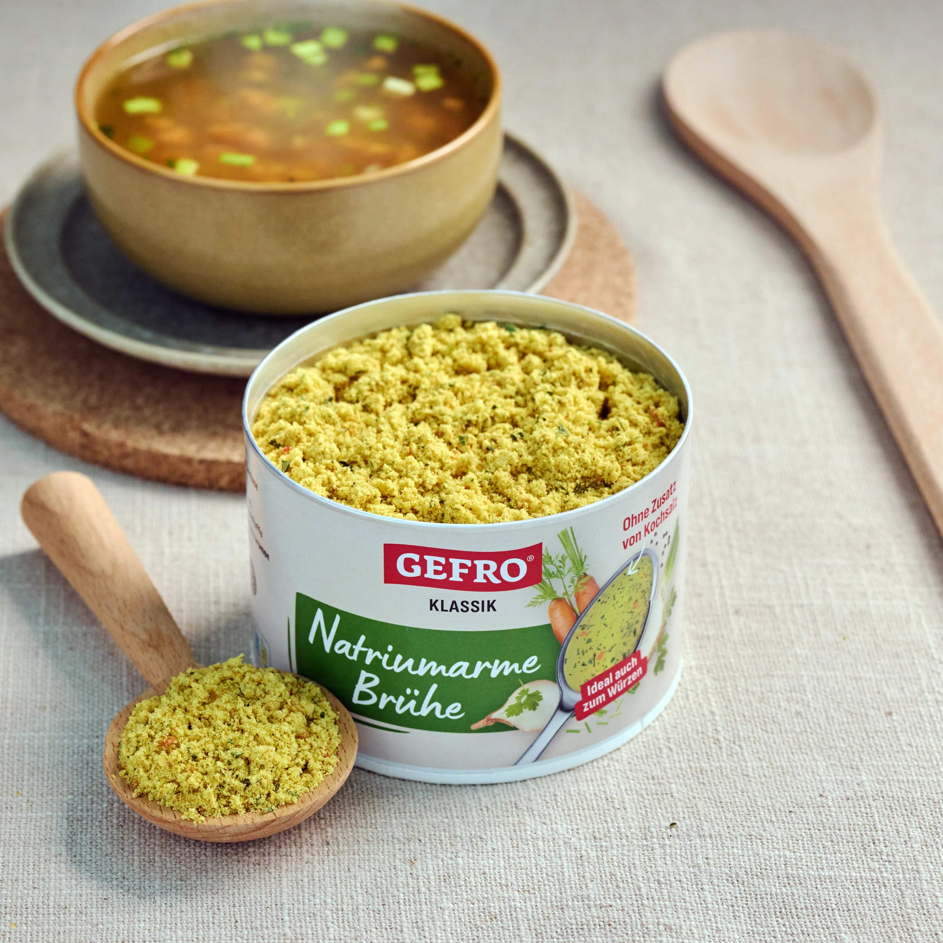 Dose mit natriumarmer Brühe von Gefro und Holzlöffel mit Pulver, daneben eine Schale mit fertiger Suppe.