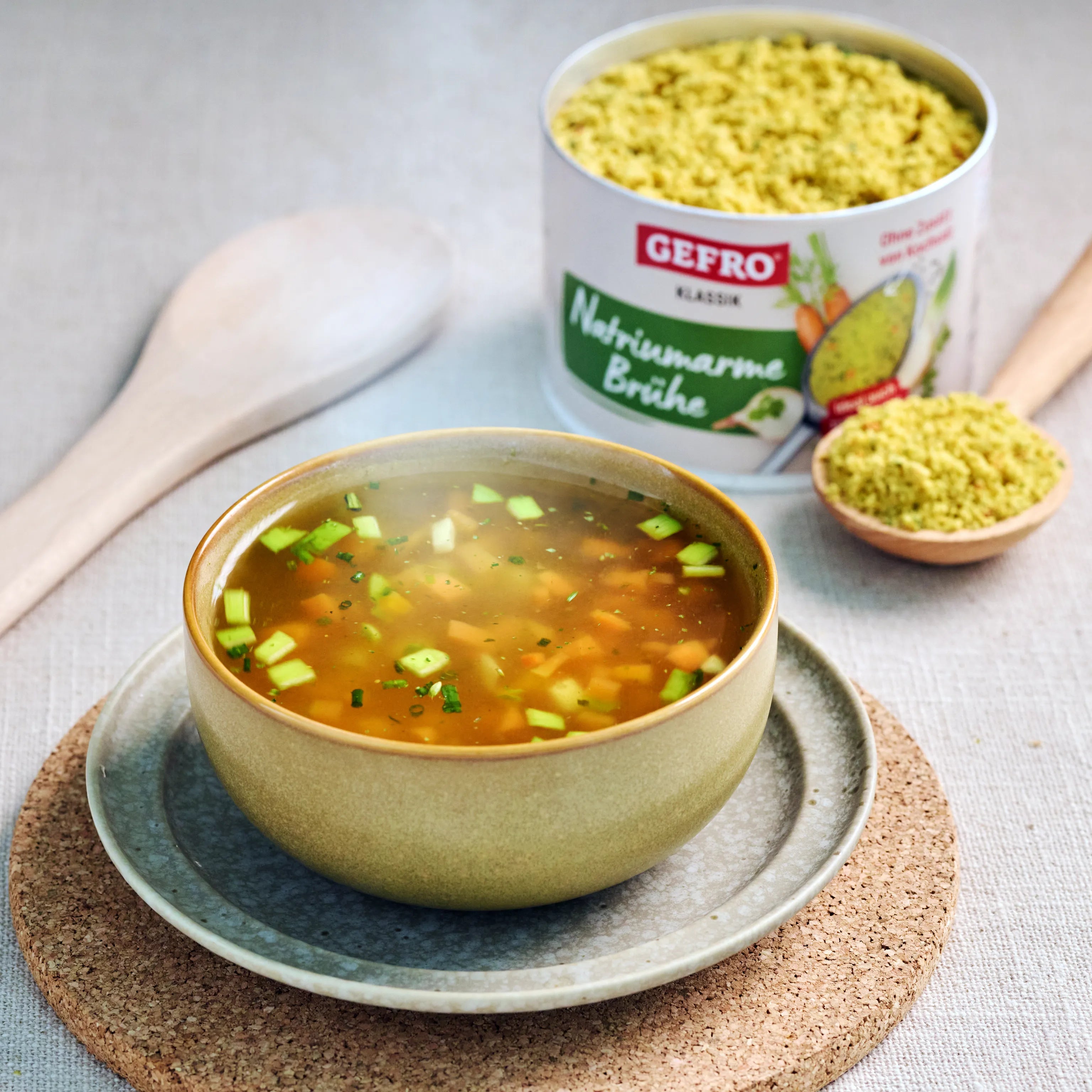 Schüssel mit klarer Gemüsesuppe auf Teller, daneben GEFRO Naturwürze Brühe und ein Löffel mit Brühpulver
