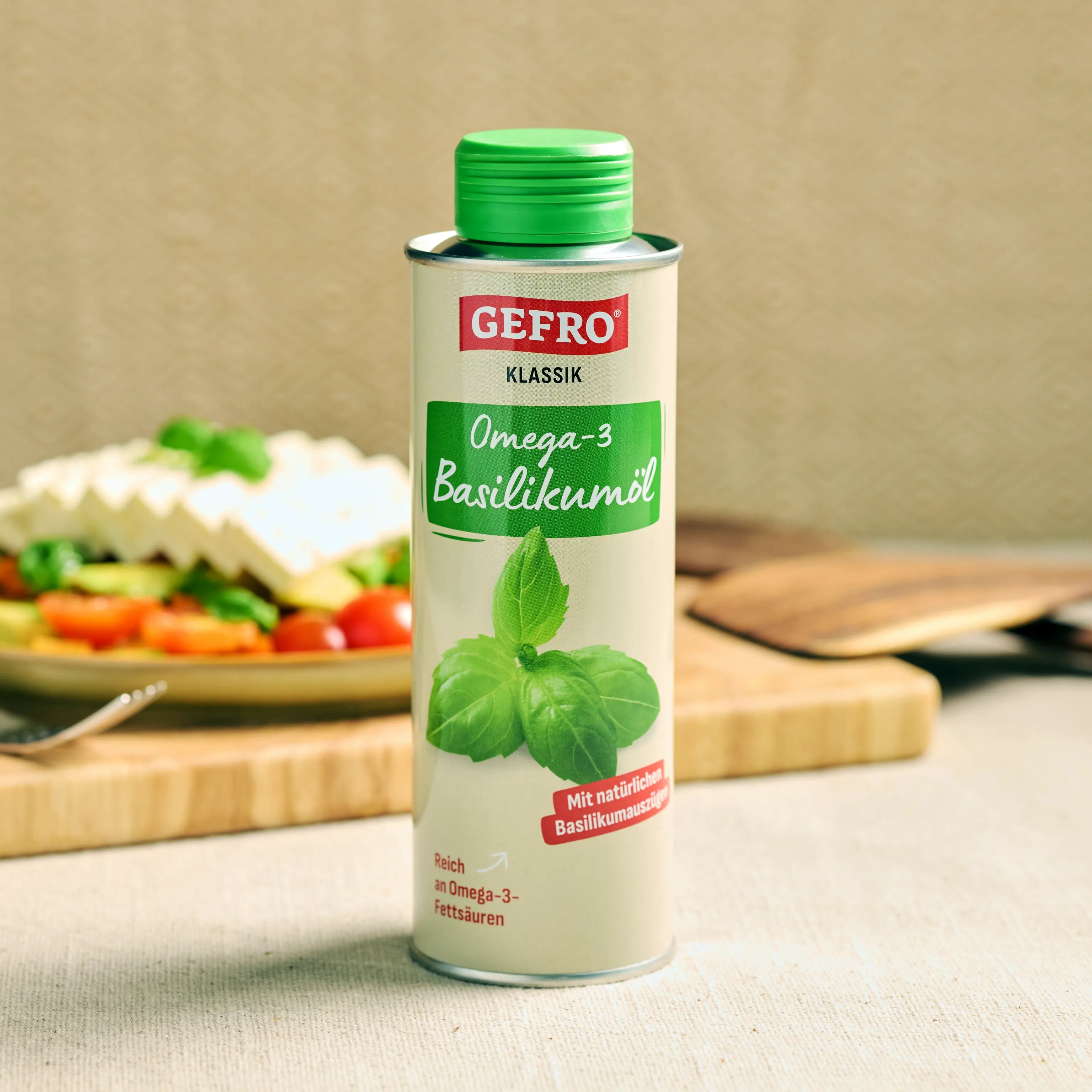 Dose GEFRO Klassik Omega-3 Basilikumöl auf Tisch, im Hintergrund Salat und Küchenbrett unscharf sichtbar