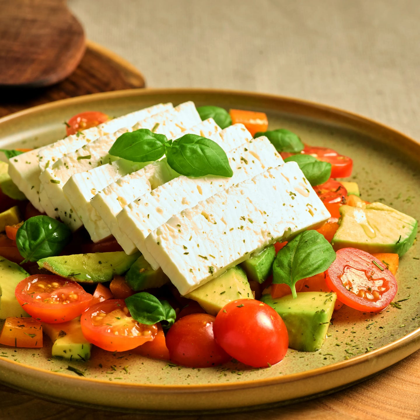 Salat mit weißen Käsewürfeln, Avocado, Cherrytomaten und frischem Basilikum auf einem Teller angerichtet