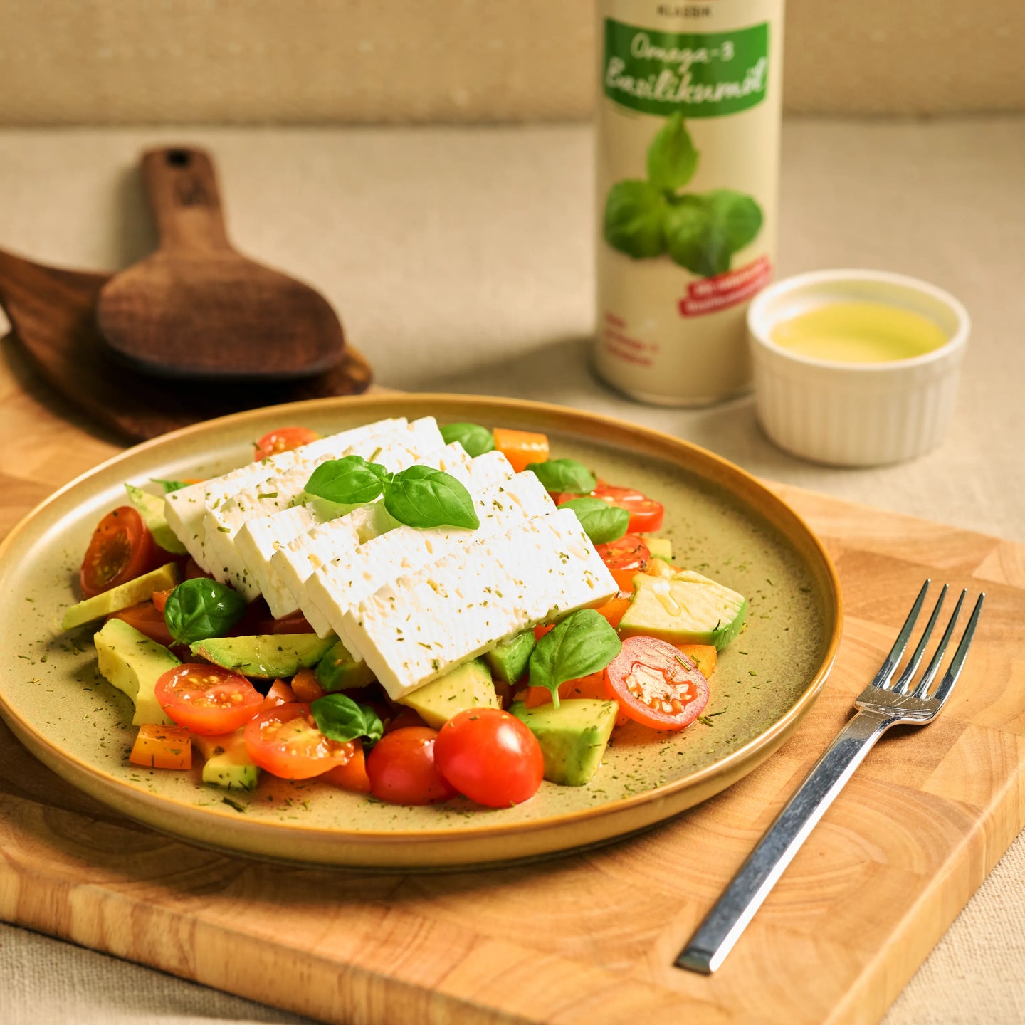 Salat mit Feta, Avocado, Tomaten und Basilikum auf einem Teller, daneben Dressing und Flasche Basilikumöl