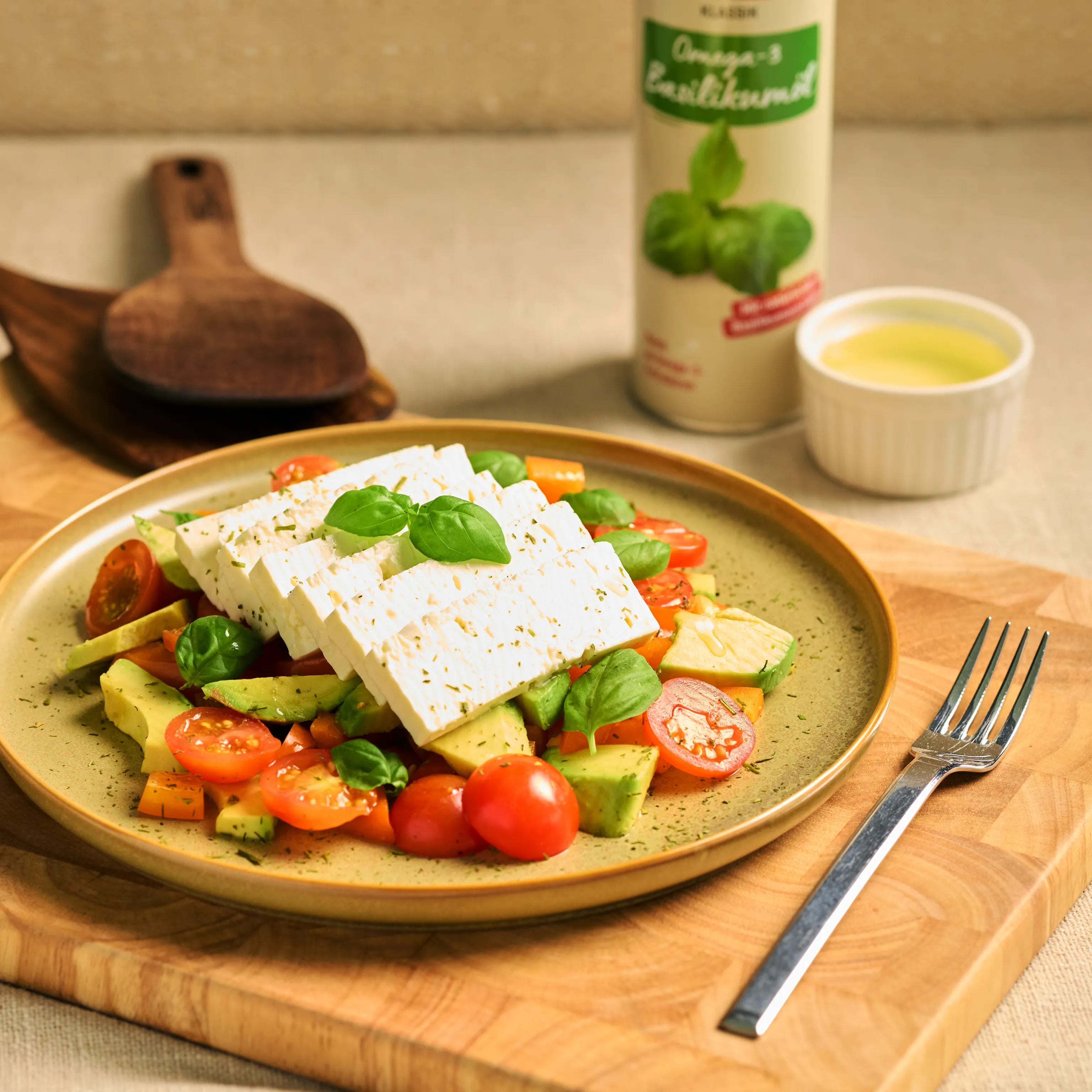 Salat mit Feta, Avocado, Tomaten und Basilikum auf einem Teller, daneben Dressing und Flasche Basilikumöl