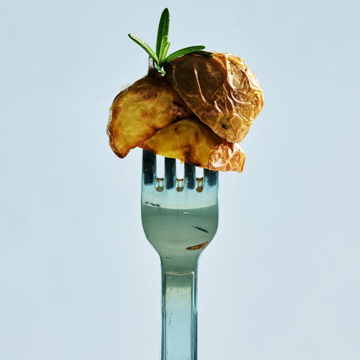 Gabel mit gebratenen Kartoffelstücken und Rosmarinzweig vor hellem Hintergrund, appetitlich angerichtet