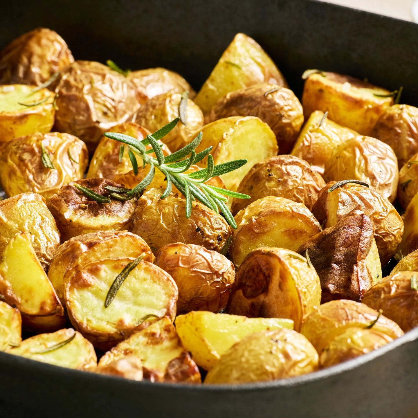Goldbraun geröstete Kartoffelhälften und kleine Kartoffeln mit Rosmarin in einer Pfanne als servierte Beilage