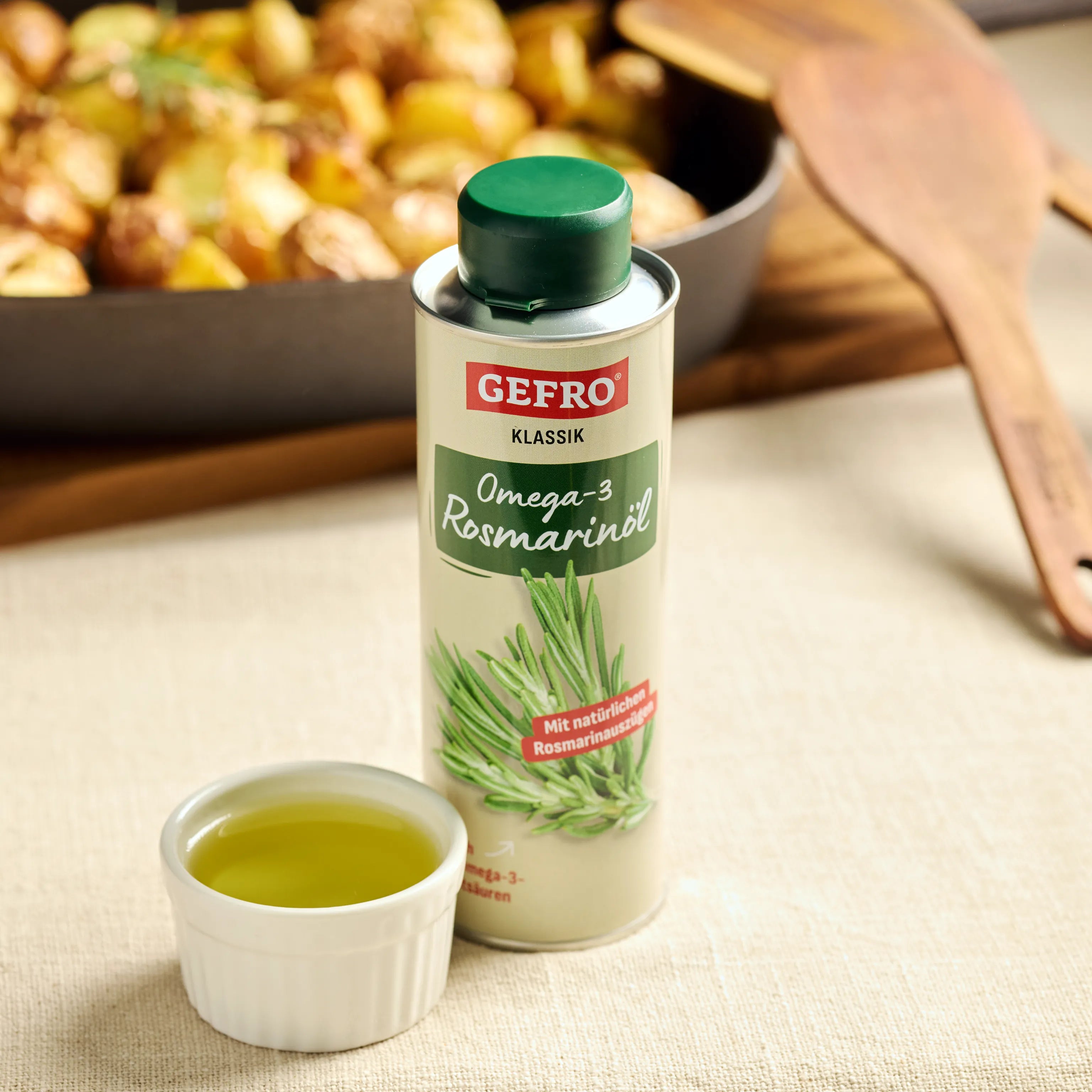 GEFRO Klassik Omega-3 Rosmarinöl mit kleinem Schälchen Öl, vor einer Pfanne mit Ofenkartoffeln auf dem Tisch