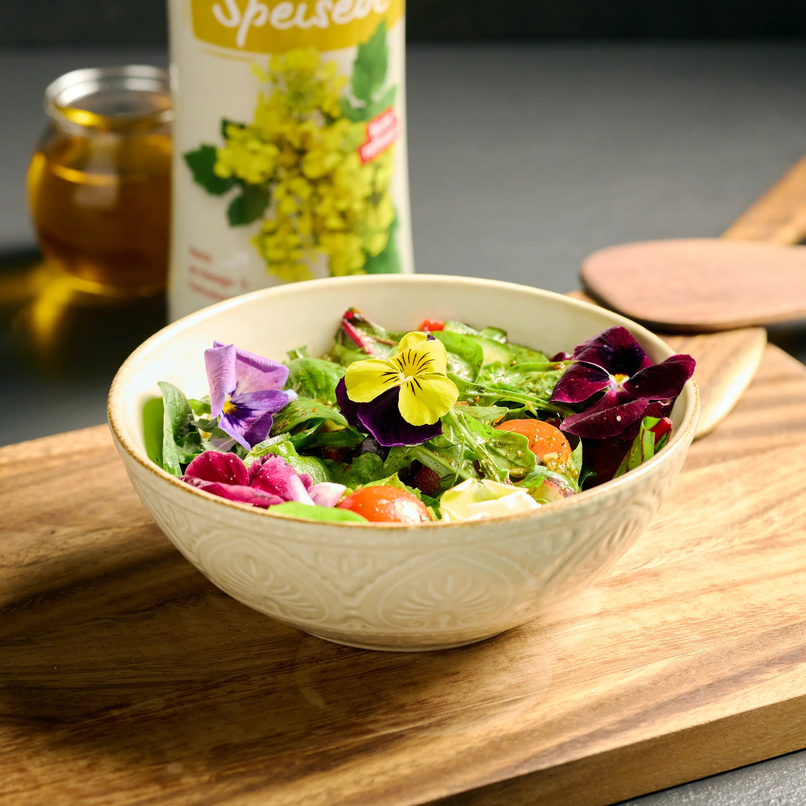 Keramikschüssel mit frischem Salat und essbaren Blüten auf Holzbrett, dekorativ serviert für den Esstisch