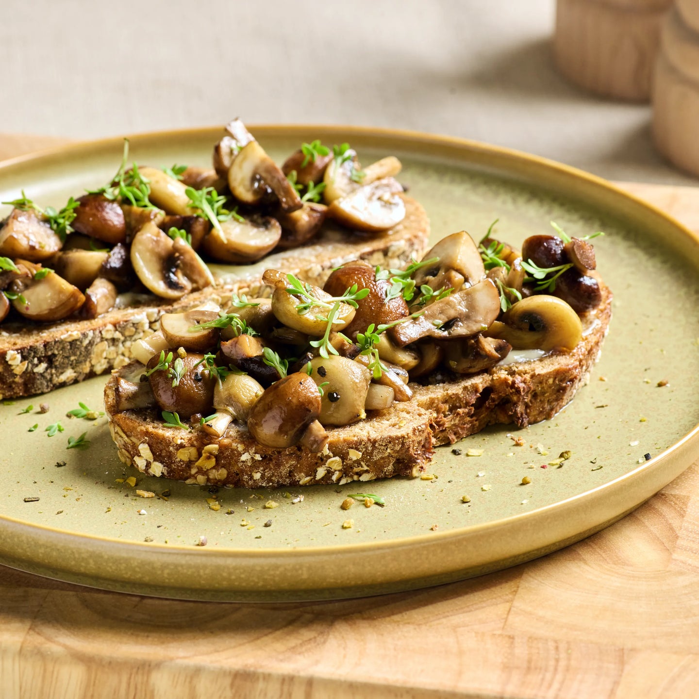 Drei Scheiben Körnerbrot mit gebratenen Champignons und frischen Kräutern auf einem großen Teller serviert