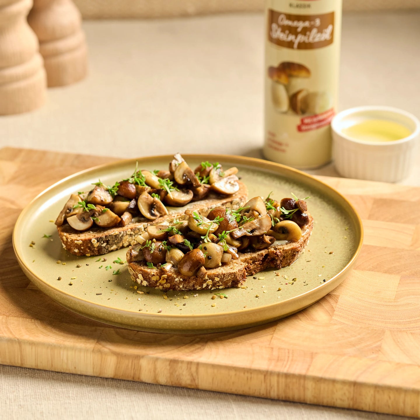 Drei Brotscheiben mit gebratenen Pilzen und Kräutern auf einem Teller, daneben Pilzöl und eine kleine Schale.