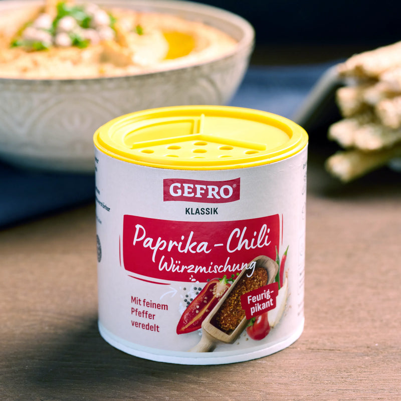 Dose GEFRO Paprika-Chili Würzmischung mit gelbem Streudeckel, davor platziert, im Hintergrund unscharfe Speisen