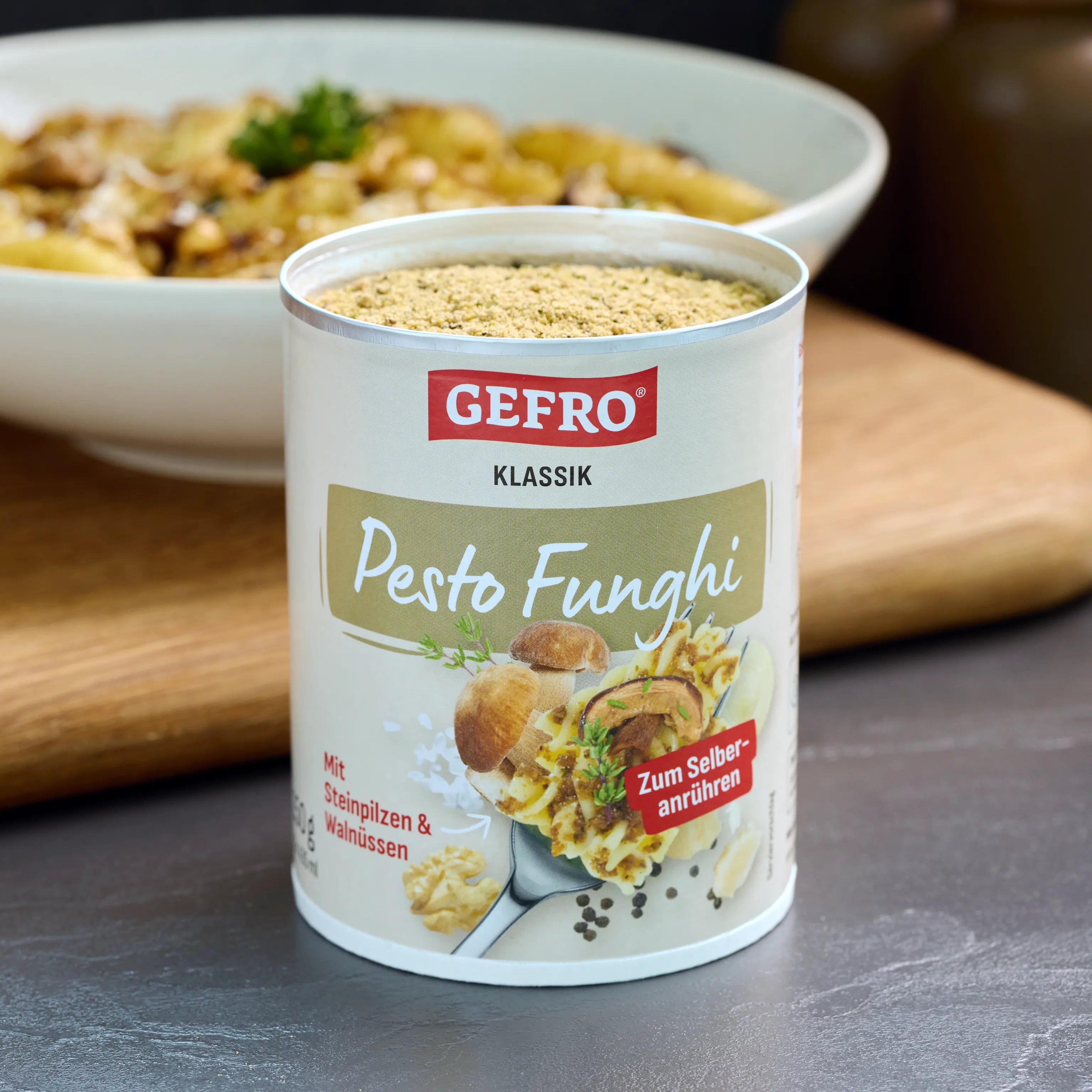 Dose GEFRO Klassik Pesto Funghi zum Anrühren, geöffnet auf Tisch, mit Pastateller im unscharfen Hintergrund