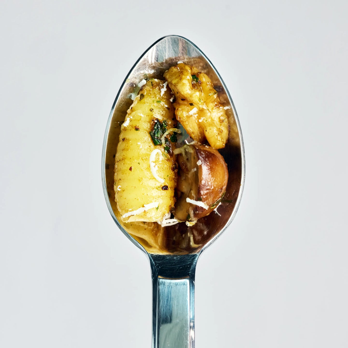 Löffel mit Gnocchi, Pilzen und geriebenem Käse in Nahaufnahme vor hellem Hintergrund