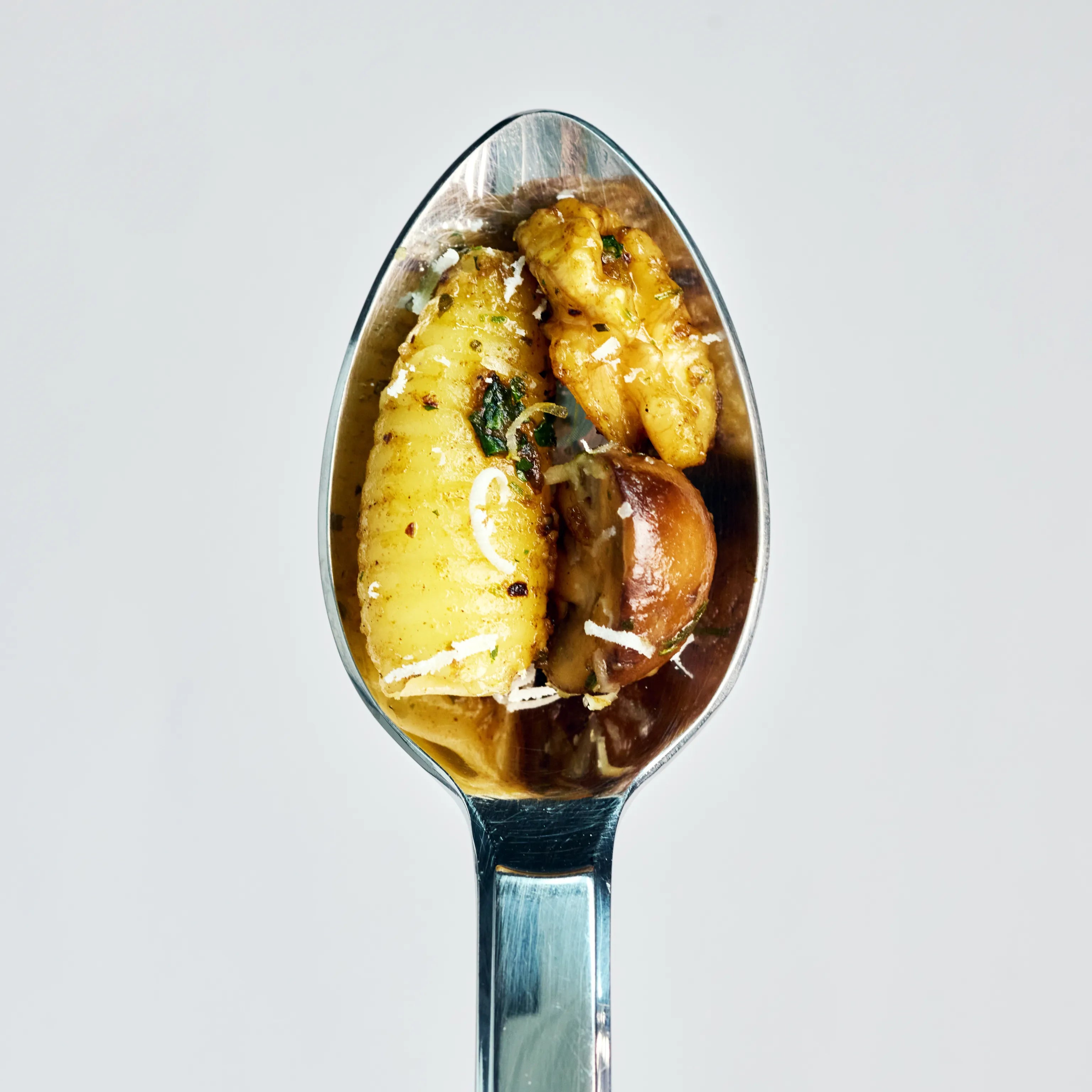 Löffel mit Gnocchi, Pilzen und geriebenem Käse in Nahaufnahme vor hellem Hintergrund