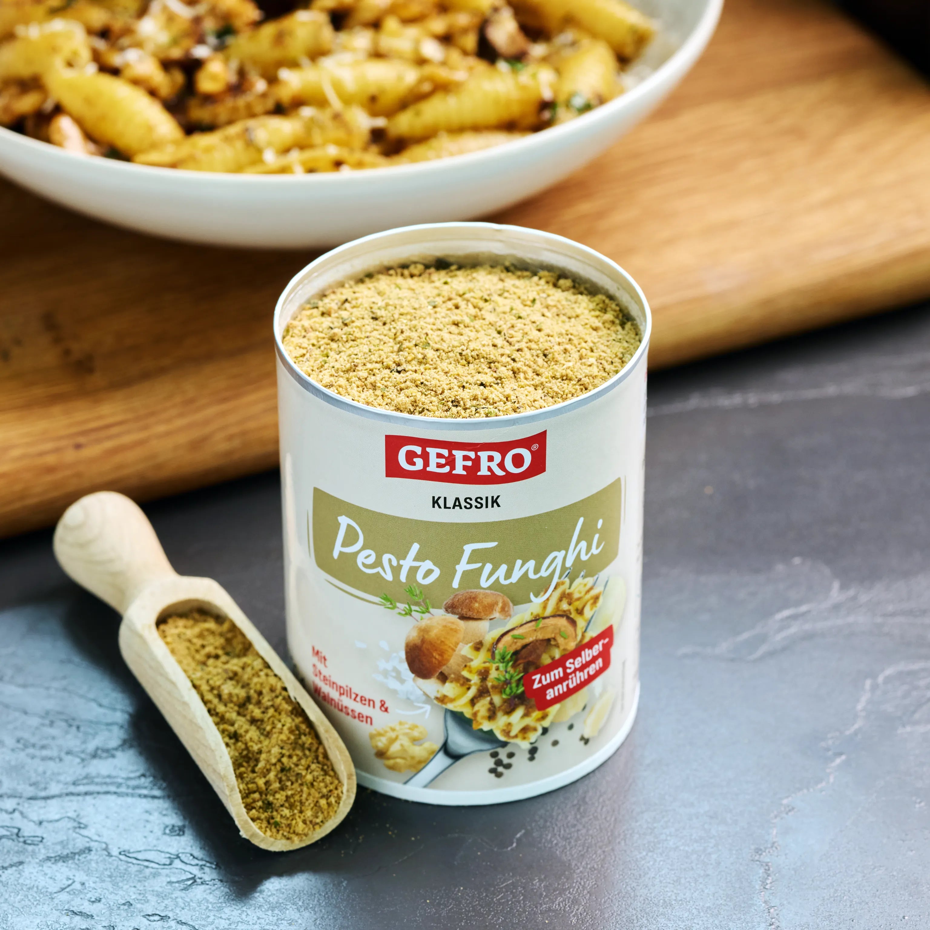 Offene Dose Gefro Pesto Funghi mit Gewürzpulver und Holzschaufel, im Hintergrund ein Teller mit Pasta auf Brett