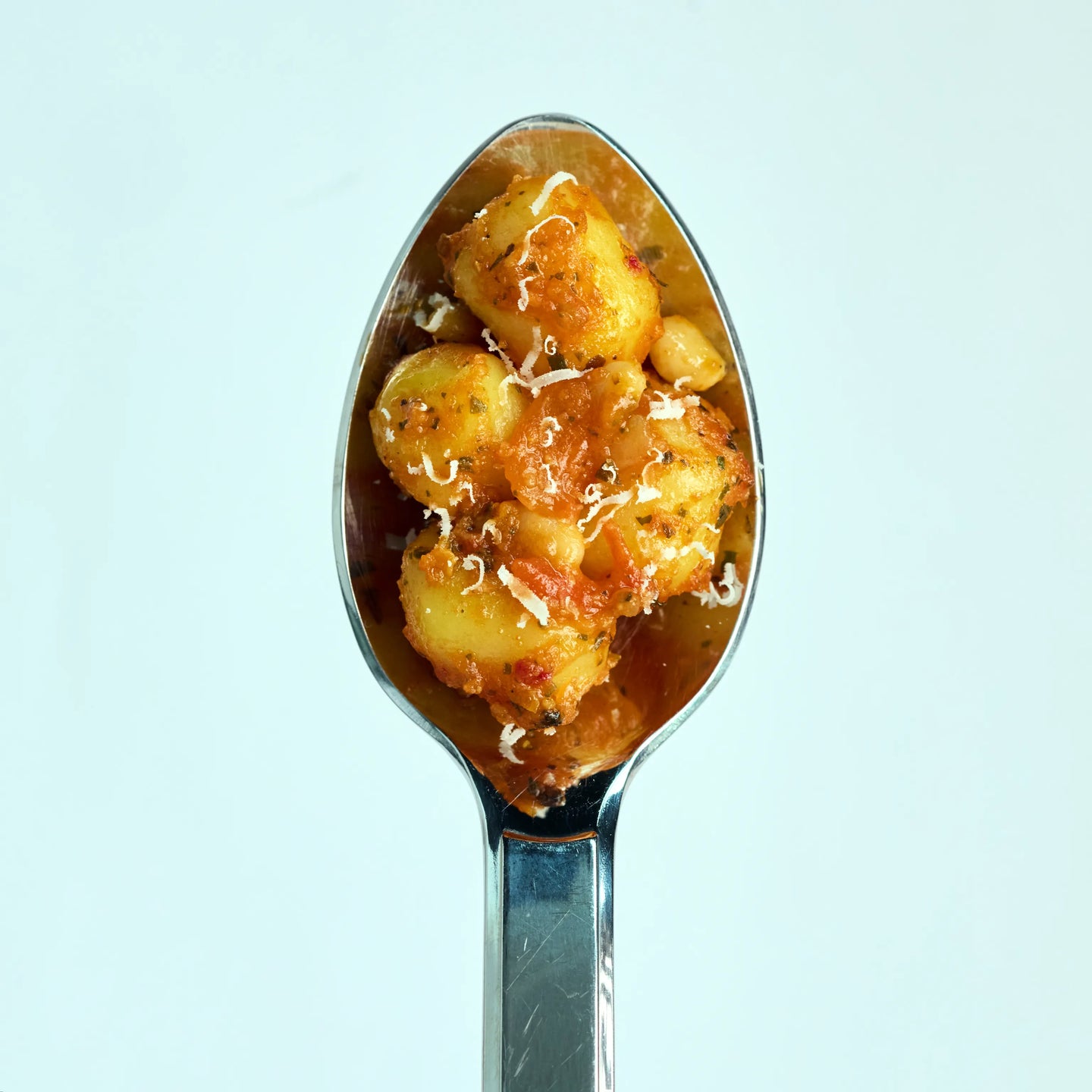 Löffel mit kleinen Gnocchi in Tomatensoße, mit Kräutern und geriebenem Käse vor hellem Hintergrund