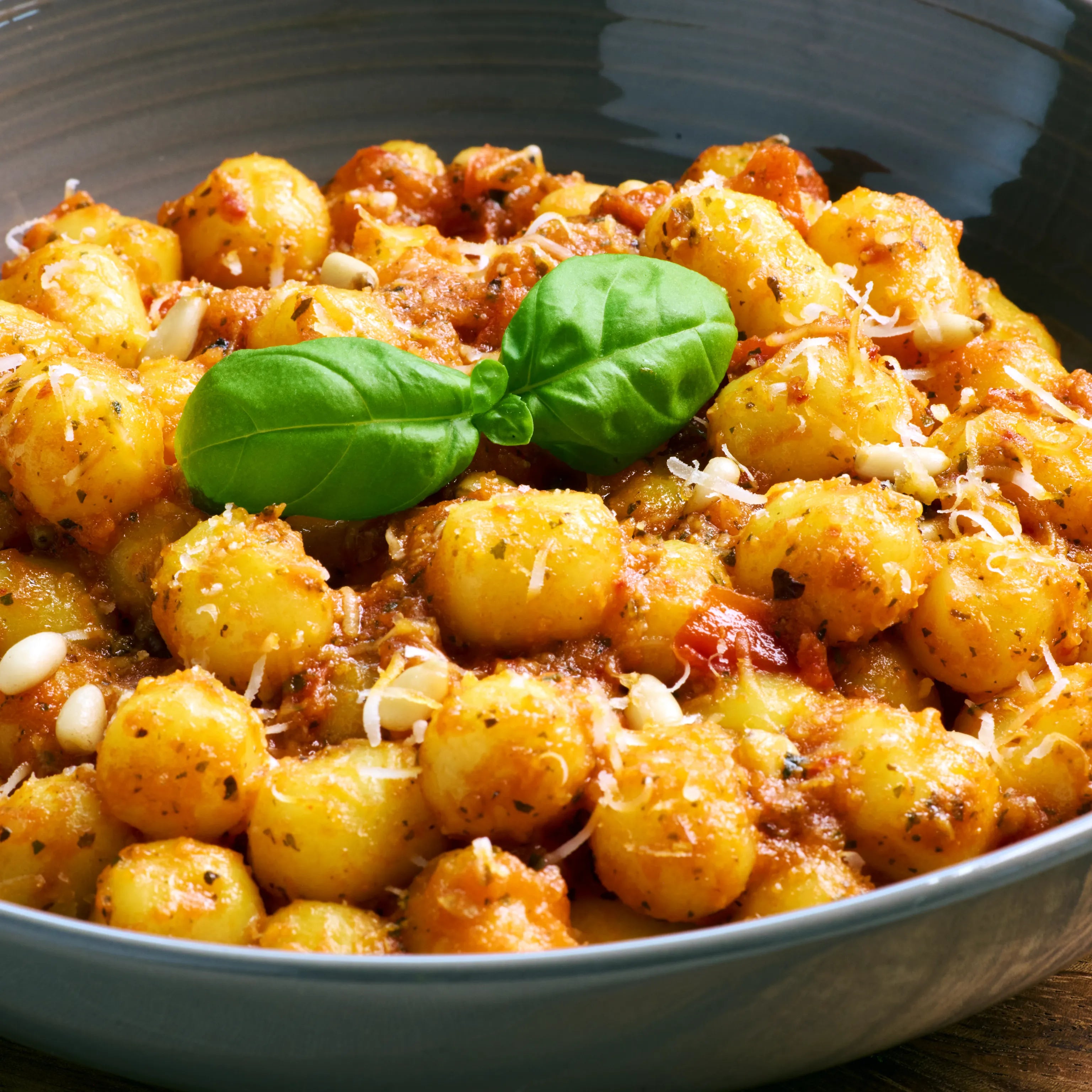 Nahaufnahme einer Schüssel Gnocchi mit Tomatensauce, geriebenem Käse, Pinienkernen und frischem Basilikum