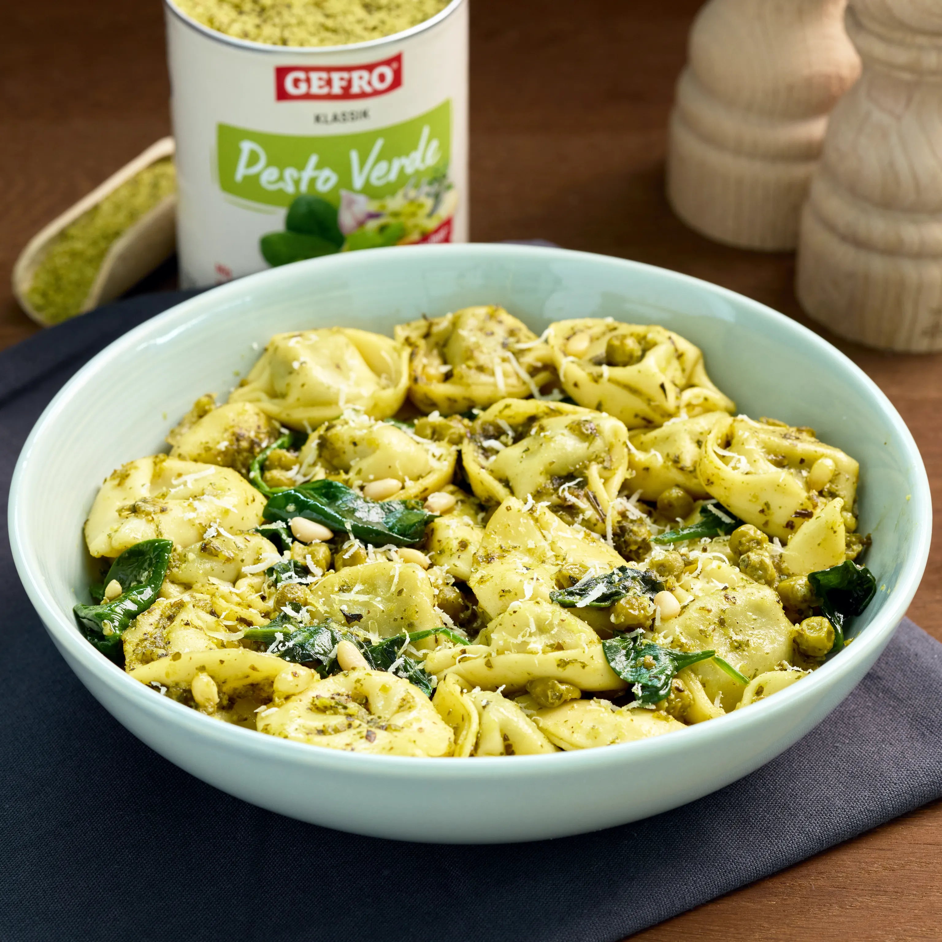 Schüssel mit Tortellini in grünem Pesto, Spinat, Erbsen, Pinienkernen und geriebenem Käse auf Holztisch