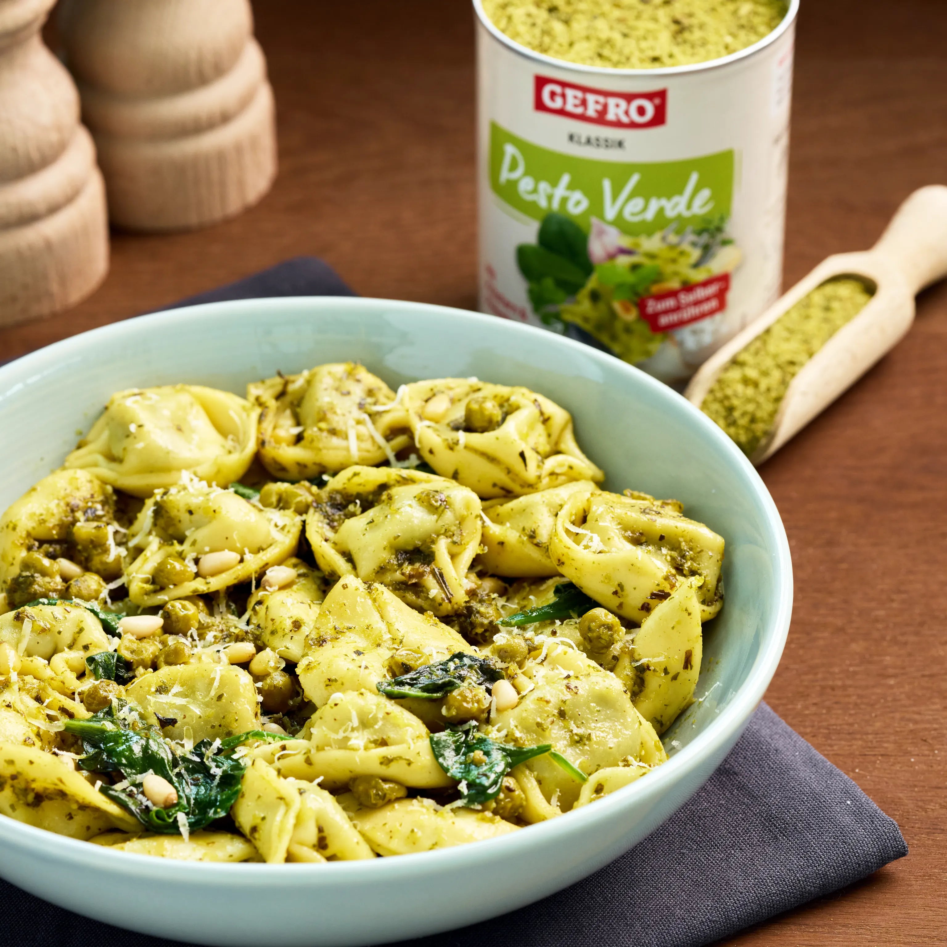 Schüssel mit Tortellini in grünem Pesto, Erbsen, Spinat und Pinienkernen, daneben Dose und Löffel mit Pesto Verde