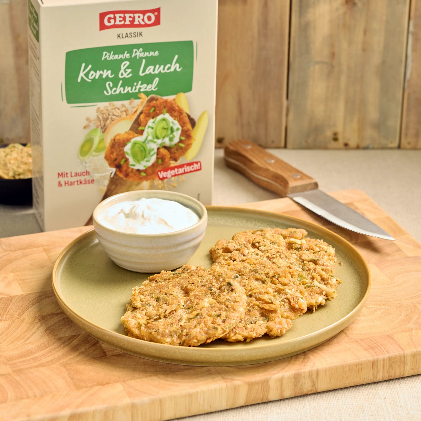 Zwei panierte Korn-Lauch-Schnitzel mit Dip auf Teller, dahinter die Packung von Gefro Klassik vegetarisch