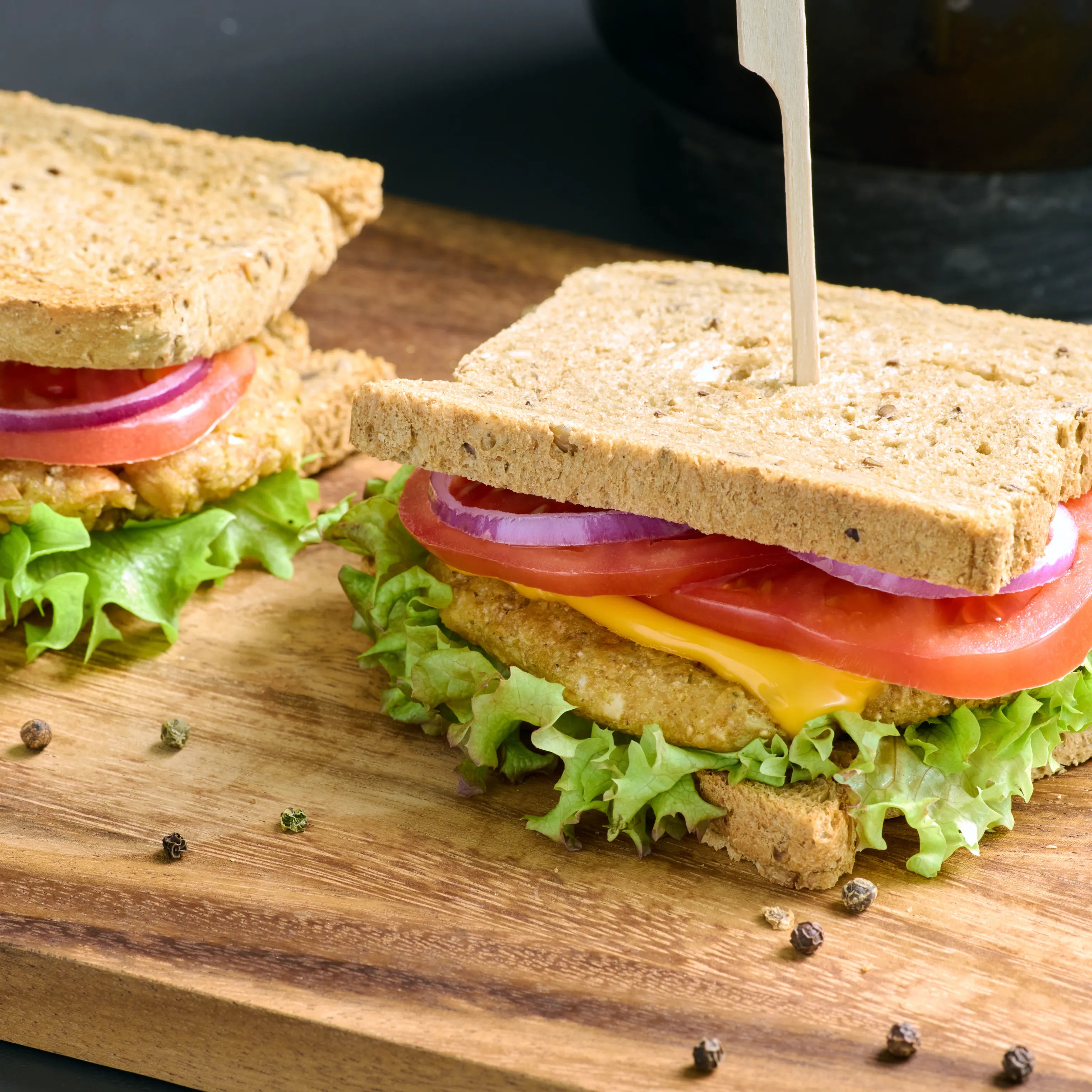 Zwei belegte Sandwiches mit Salat, Tomaten, roten Zwiebeln, Käse und paniertem Patty auf einem Holzbrett.