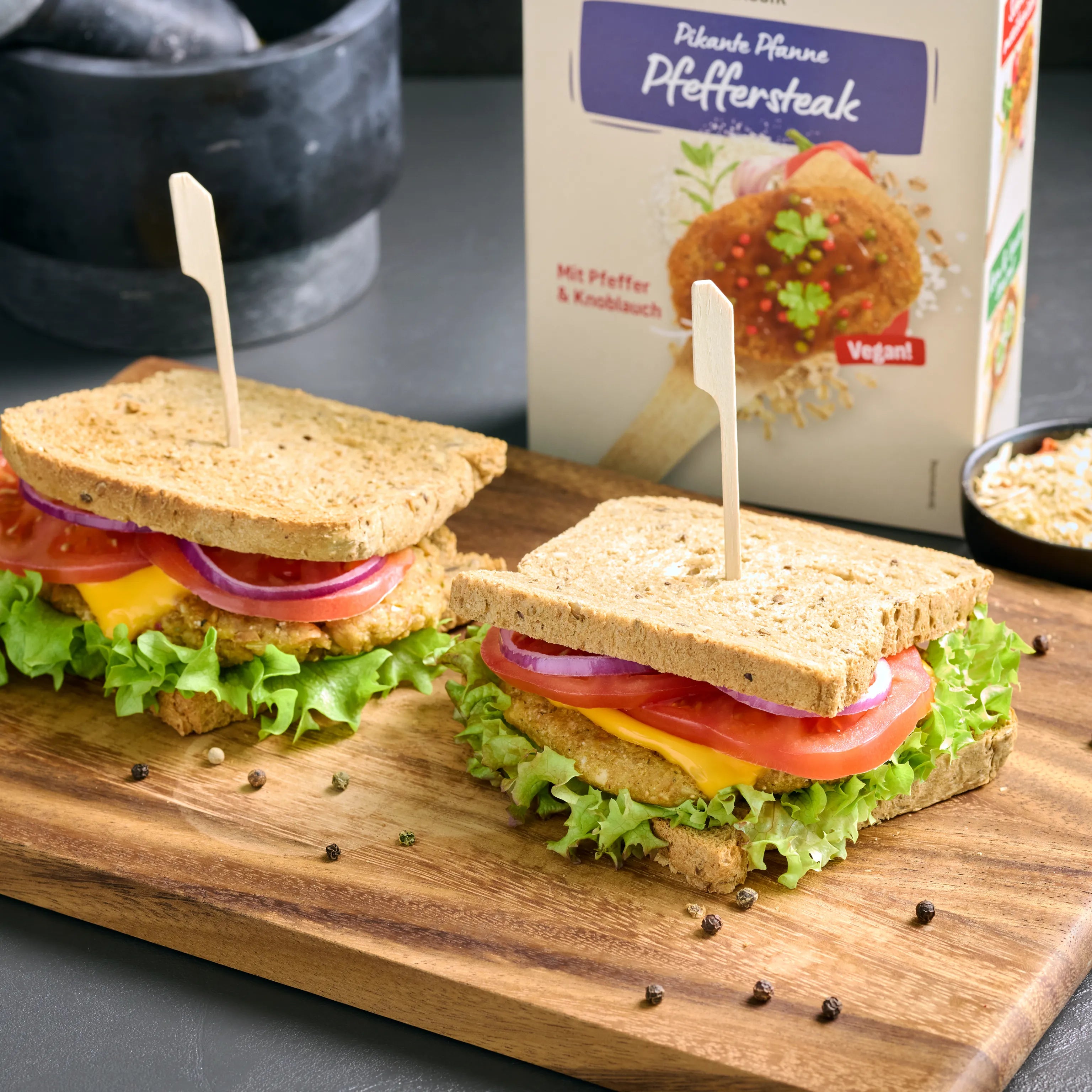 Zwei belegte Sandwiches mit Salat, Tomate, Zwiebeln und veganem Pfeffersteak auf einem Holzbrett serviert
