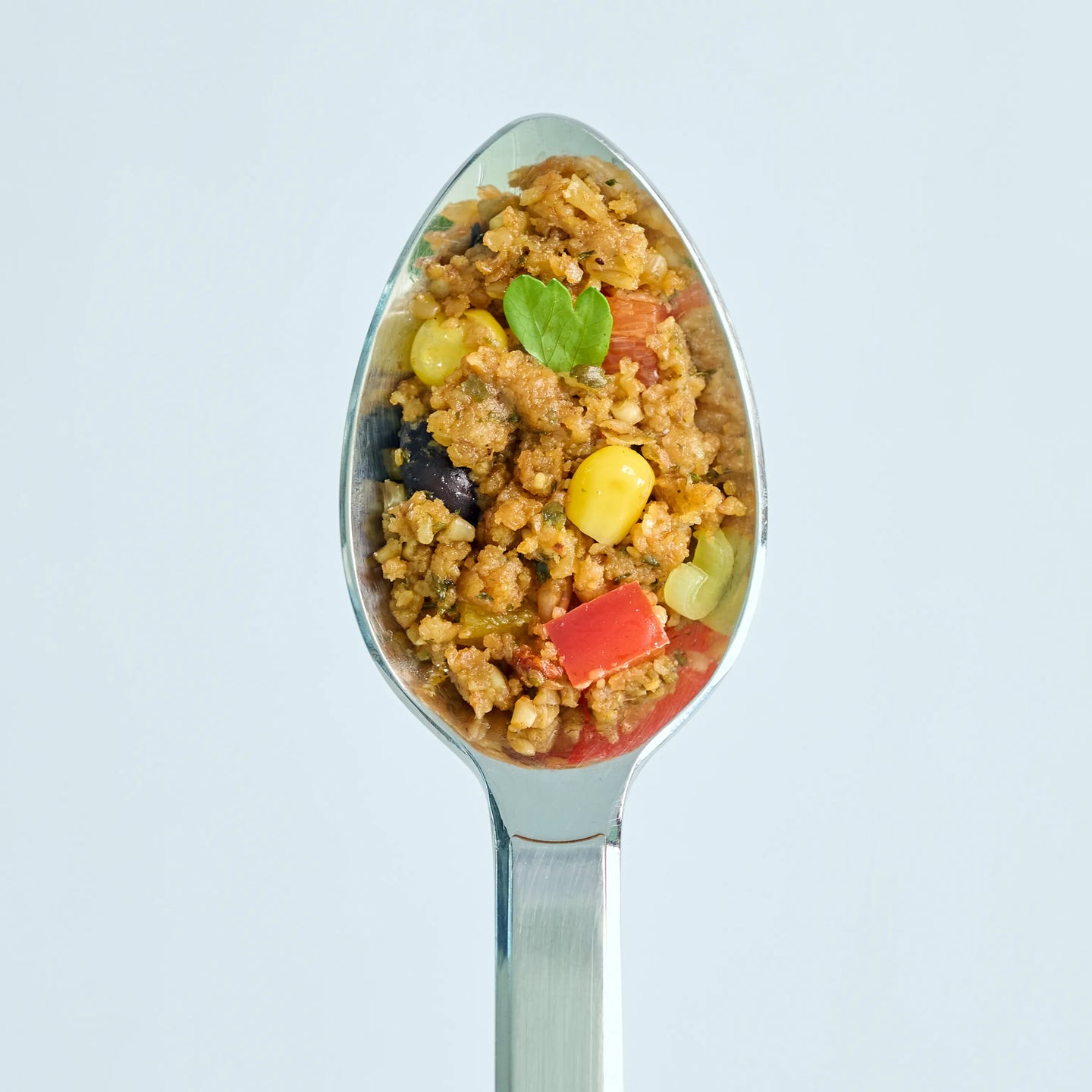 Löffel mit würziger Gemüsefüllung aus Mais, Paprika, Oliven und Kräutern vor hellem Hintergrund