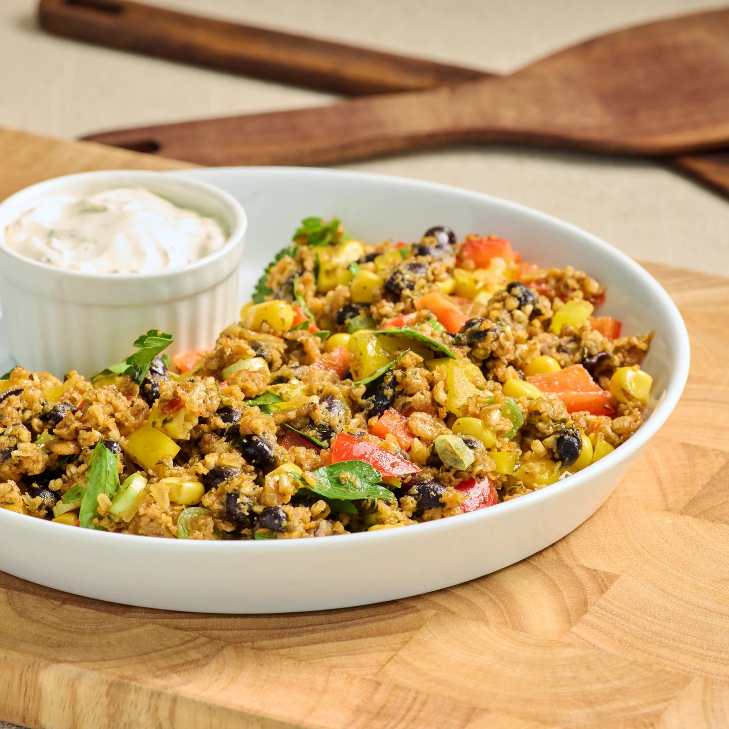 Schüssel mit würzigem Salat aus schwarzen Bohnen, Mais und Paprika, dazu ein kleiner Becher mit cremigem Dip.