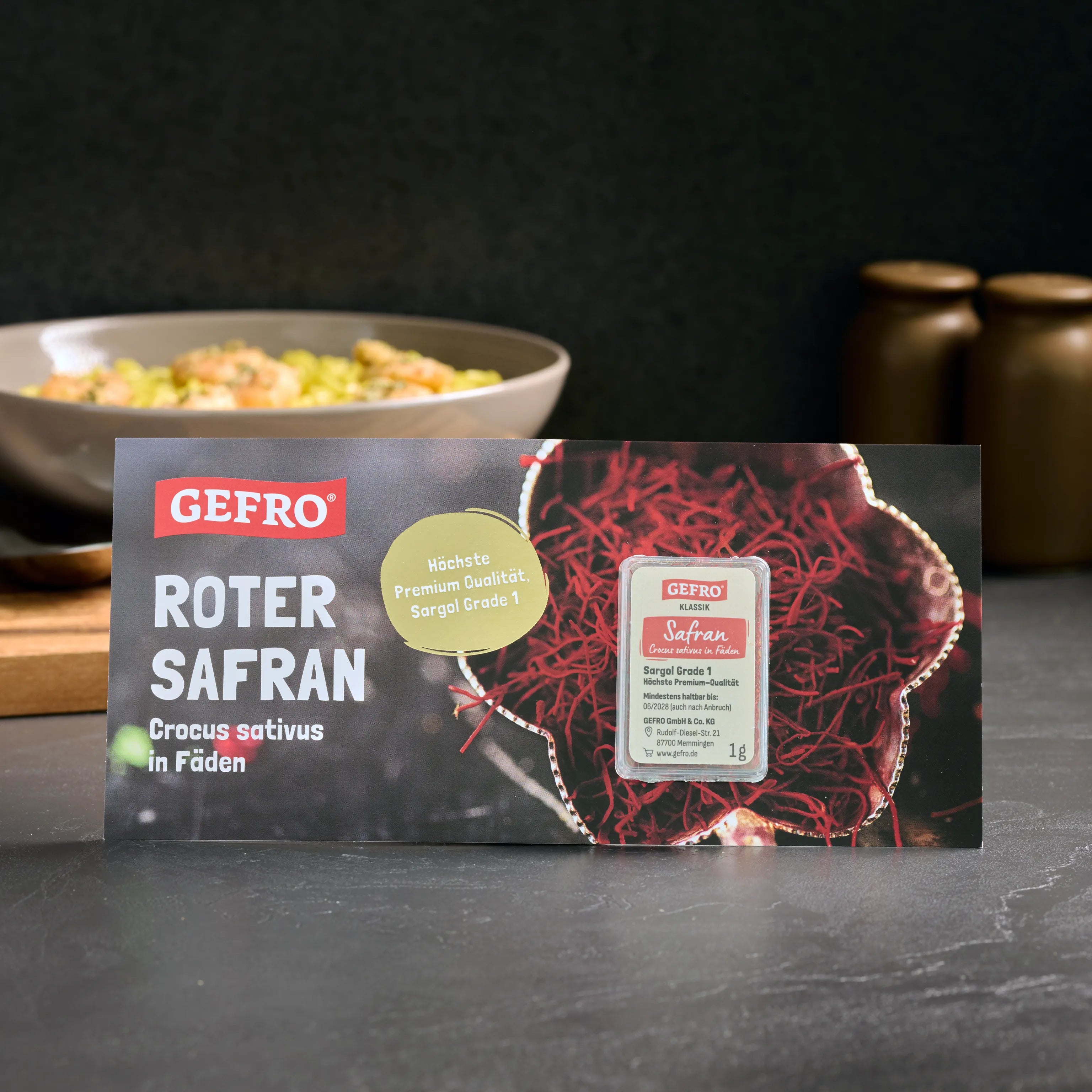 Verpackung von GEFRO Roter Safran in Fäden, 1 g, vor dunklem Hintergrund mit Schale im unscharfen Hintergrund